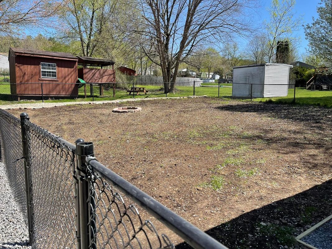 A fenced backyard with dirt and sparse grass, a small shed, and a fire pit.