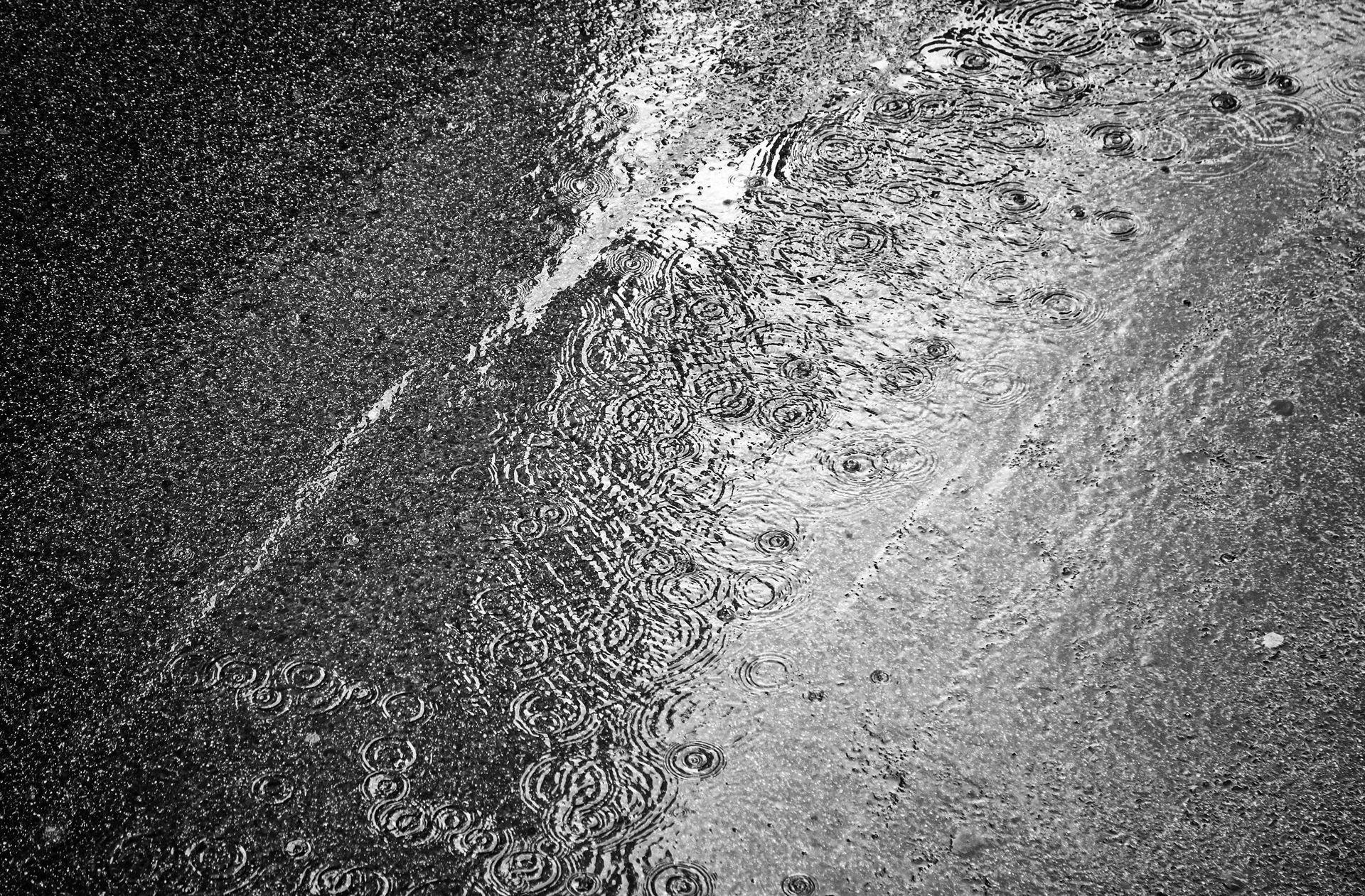 Ripples on a wet, dark pavement surface, with light reflecting off the water.