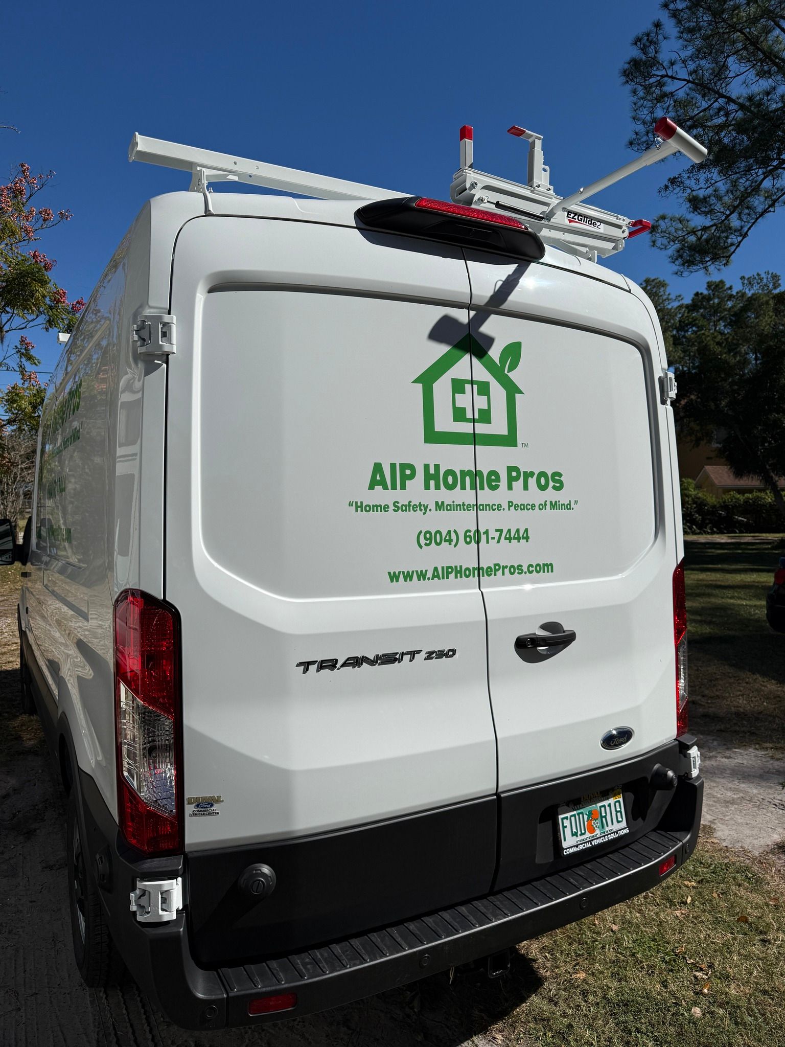 White service van with roof ladders and green “AIP Home Pros” logo parked outdoors in sunlight