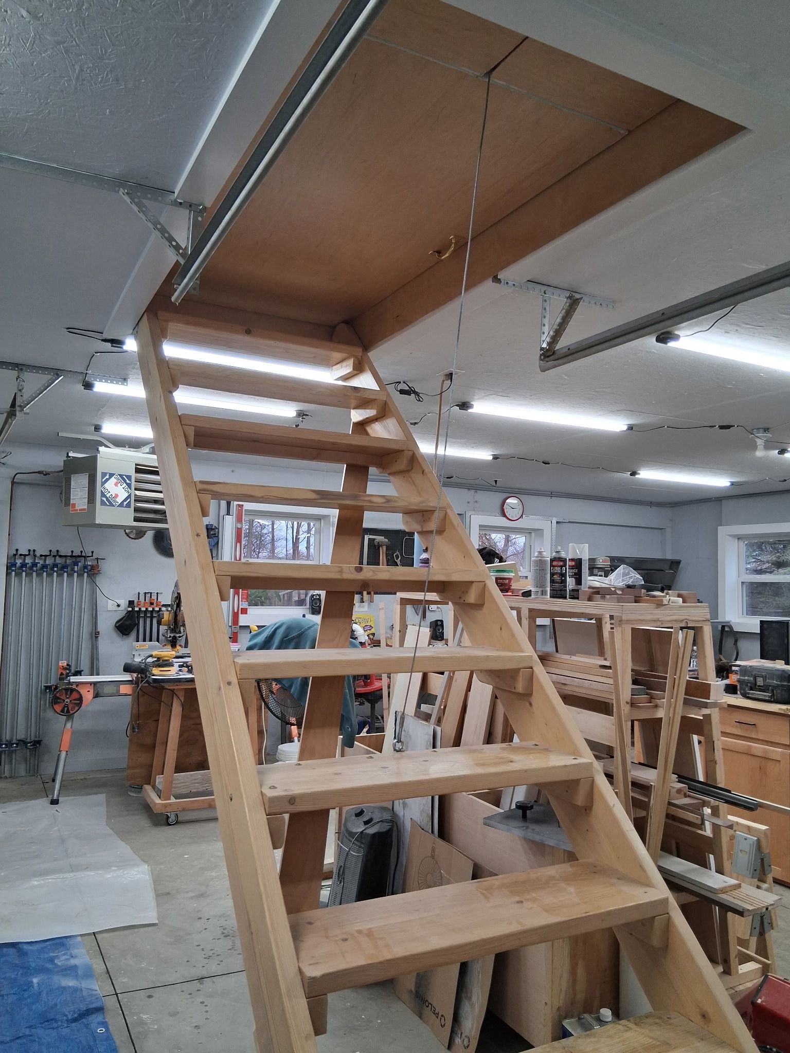Wooden stairs leading to a loft in a workshop or furniture store, with shelves and tools in the background