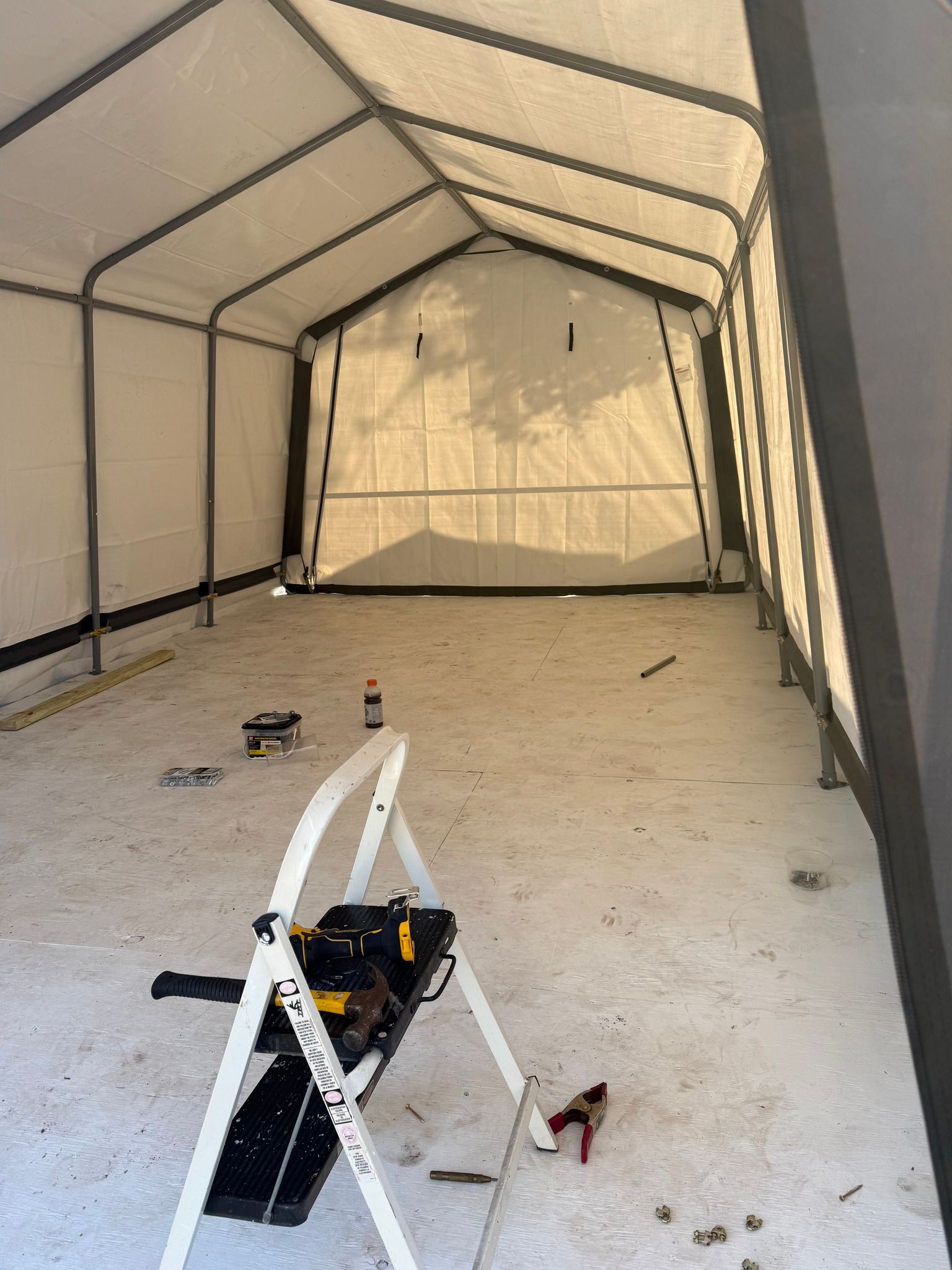 Inside an empty white tent, with a small toolbox and ladder on the floor.