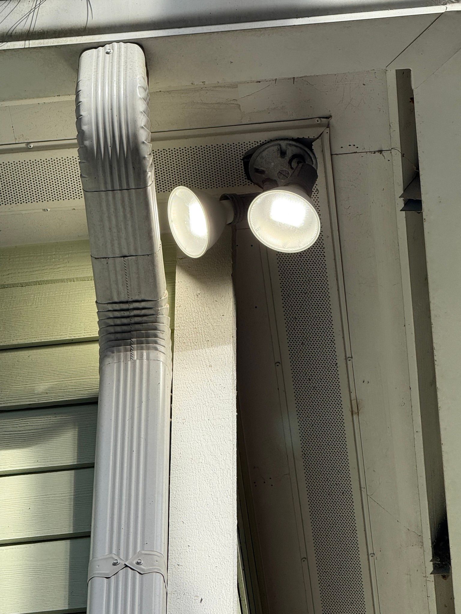 Two bright spotlights mounted beside a doorway, with a vertical downspout on the left.