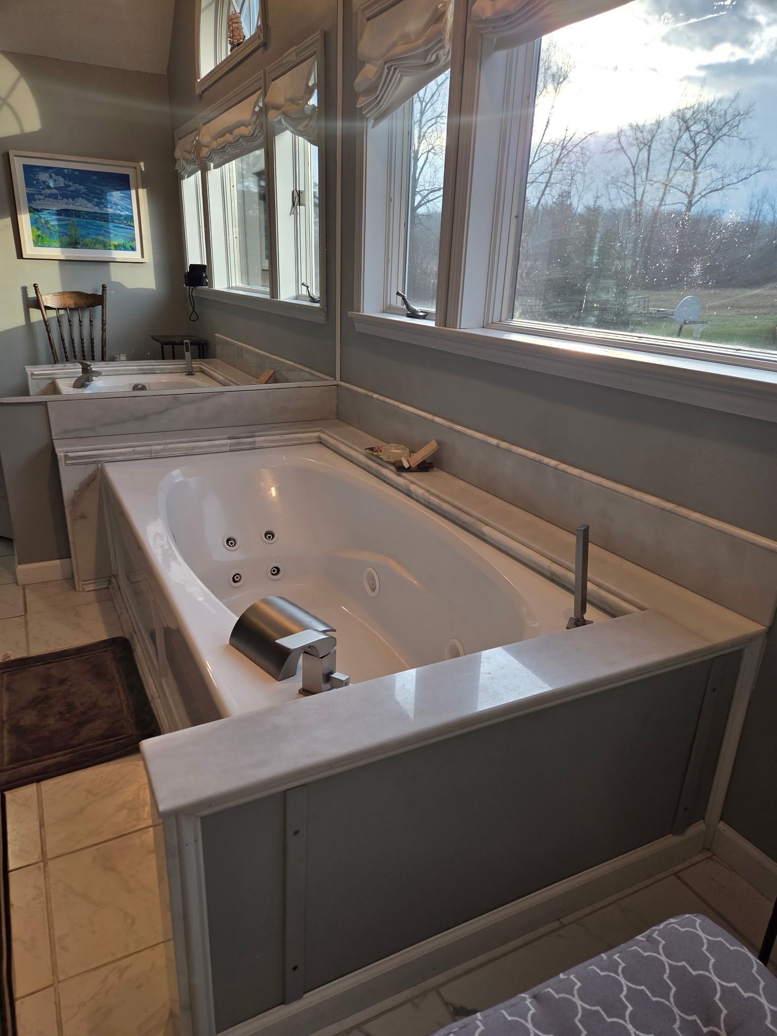 Bathroom showroom with a white soaking tub, gray paneling, and large windows overlooking trees.