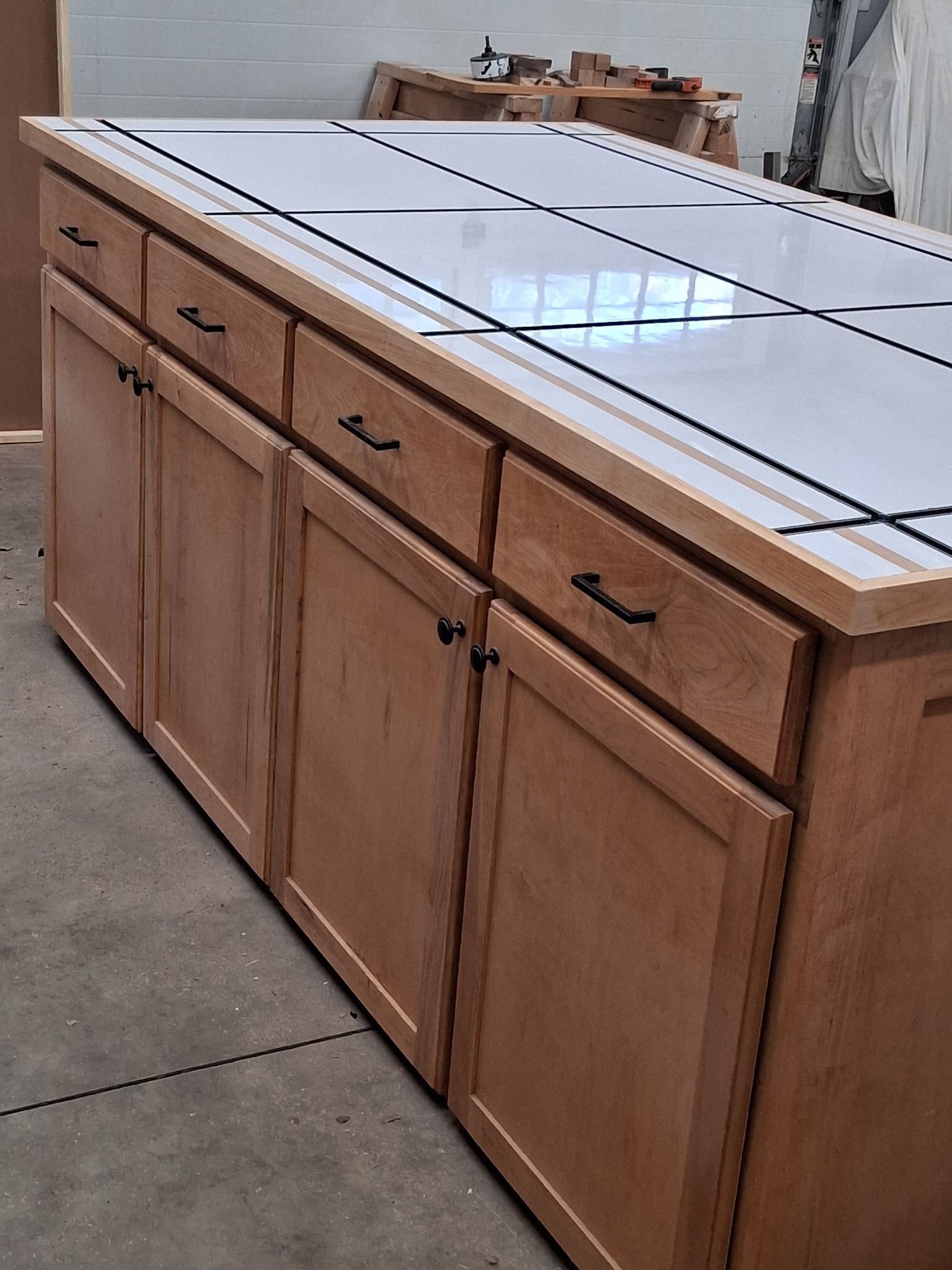 Wooden kitchen island cabinet with white tiled countertop in a workshop area