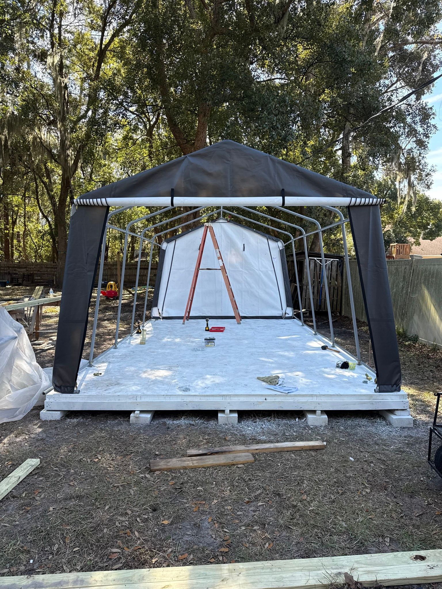 Black canopy tent with string lights and white backdrop on a wooden platform in a wooded yard