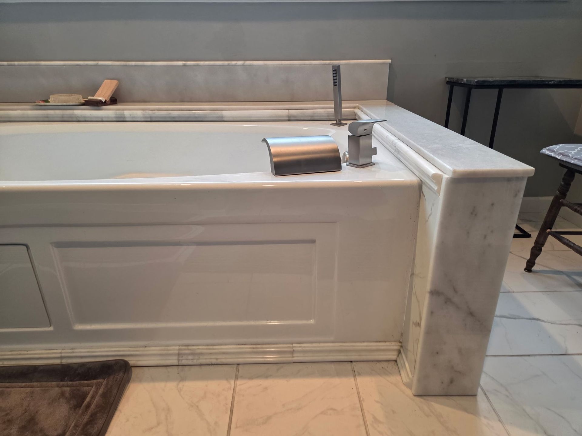 Marble bathroom vanity with built-in bathtub, faucet, soap dispenser, and a brown bath mat