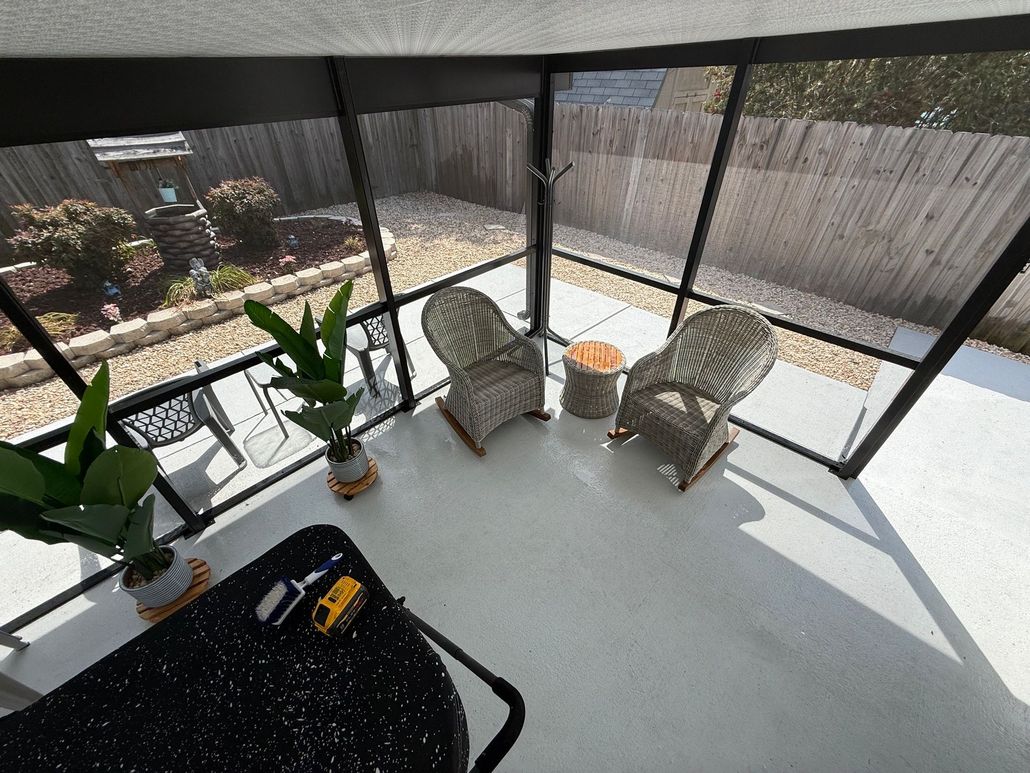 Sunlit screened patio with two wicker chairs, potted plants, and a black table by a fenced yard