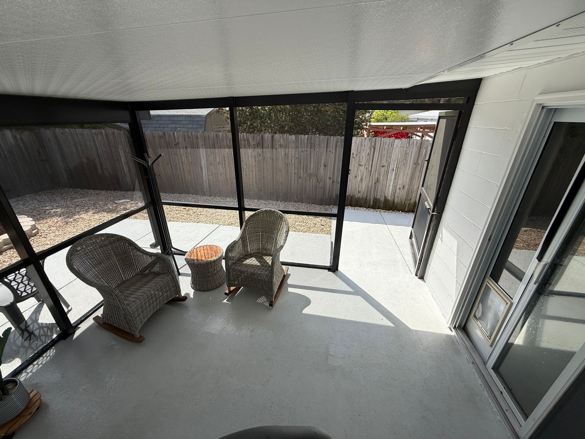 Screened patio with wicker chairs, a small table, and sliding glass doors in bright sunlight