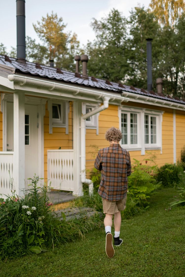 Child walking toward a yellow house with a white porch and green lawn
