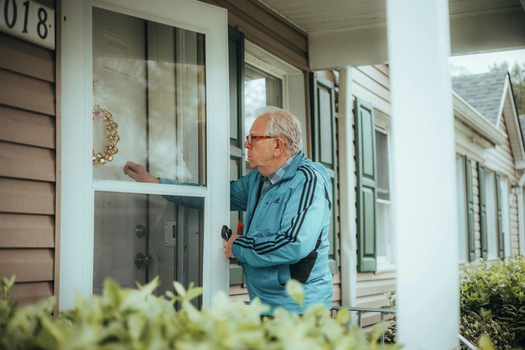 Man in a blue jacket knocking on a front door of a house.