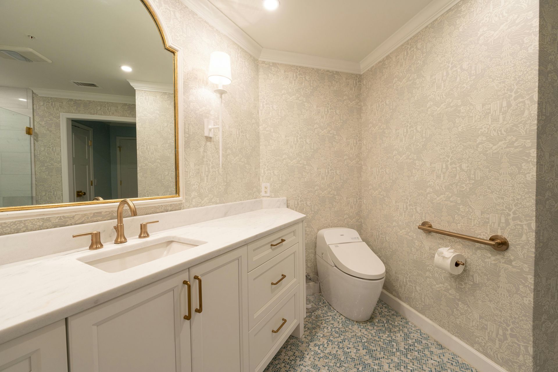 Bright bathroom with vanity, large mirror, toilet, and textured wallpaper, in cream and gold tones