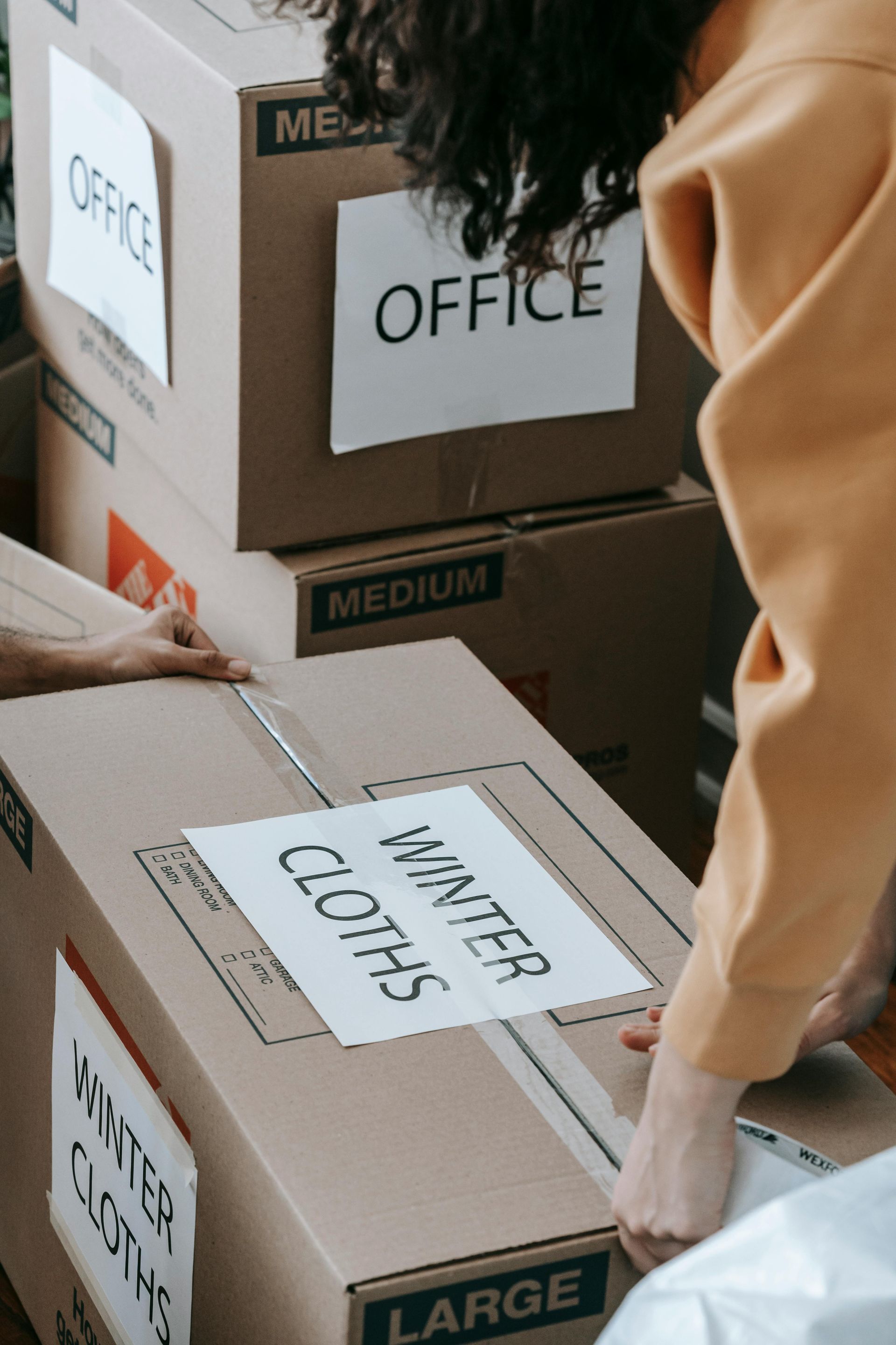 Person packing labeled moving boxes marked office, kitchen, medium, and large.