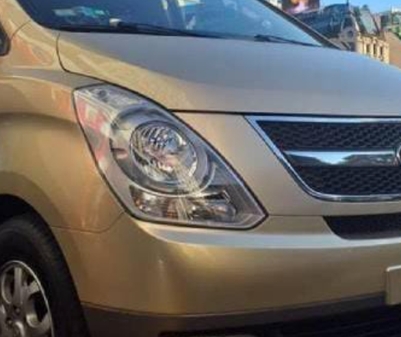 Esquina delantera de un SUV beige con faro y parrilla, estacionado en una calle.