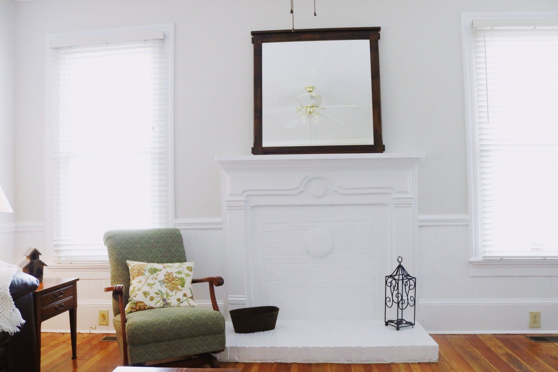 White room with fireplace, mirror, and green armchair.