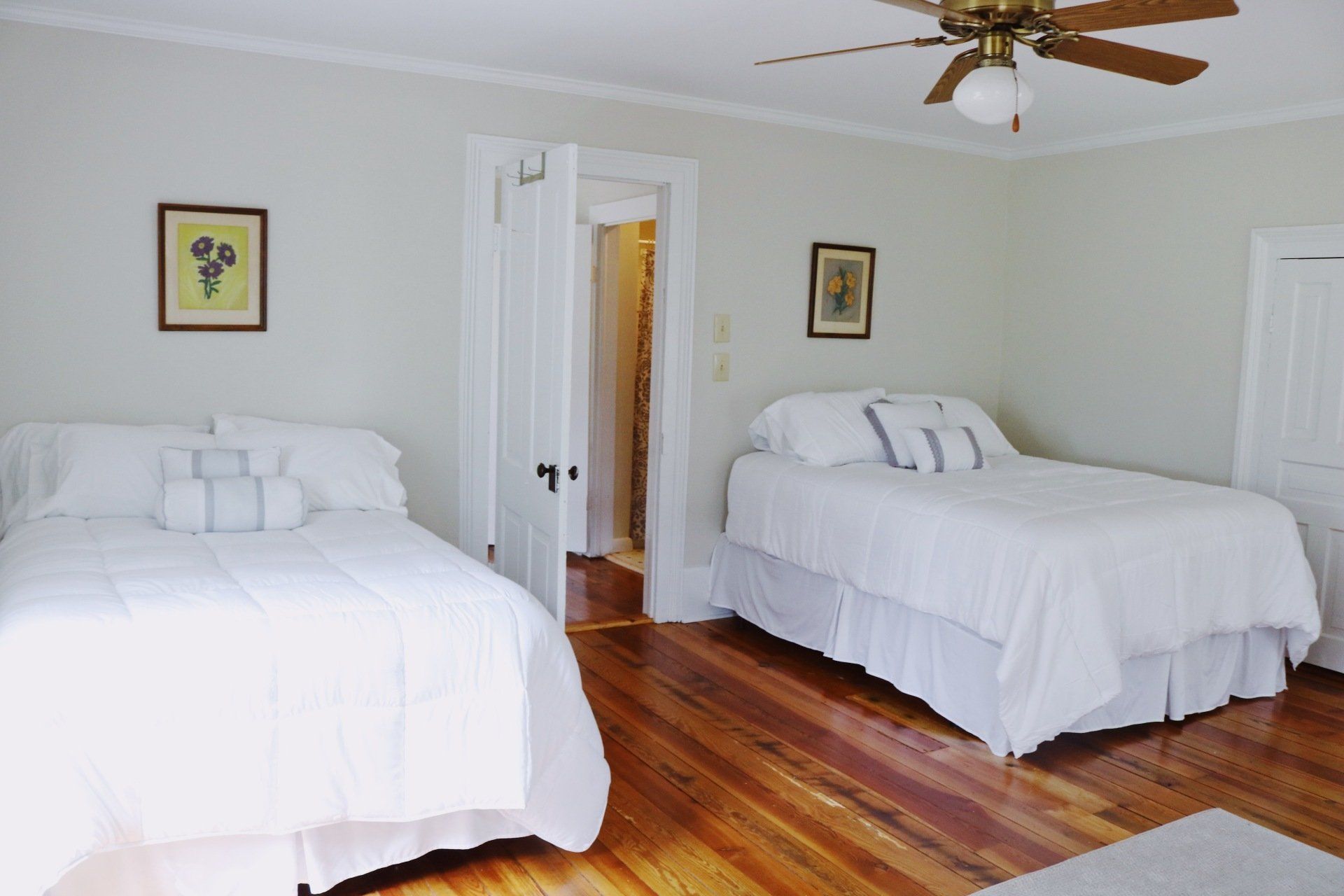 Bedroom with two twin beds, white bedding, hardwood floor, light green walls, ceiling fan, and open door.