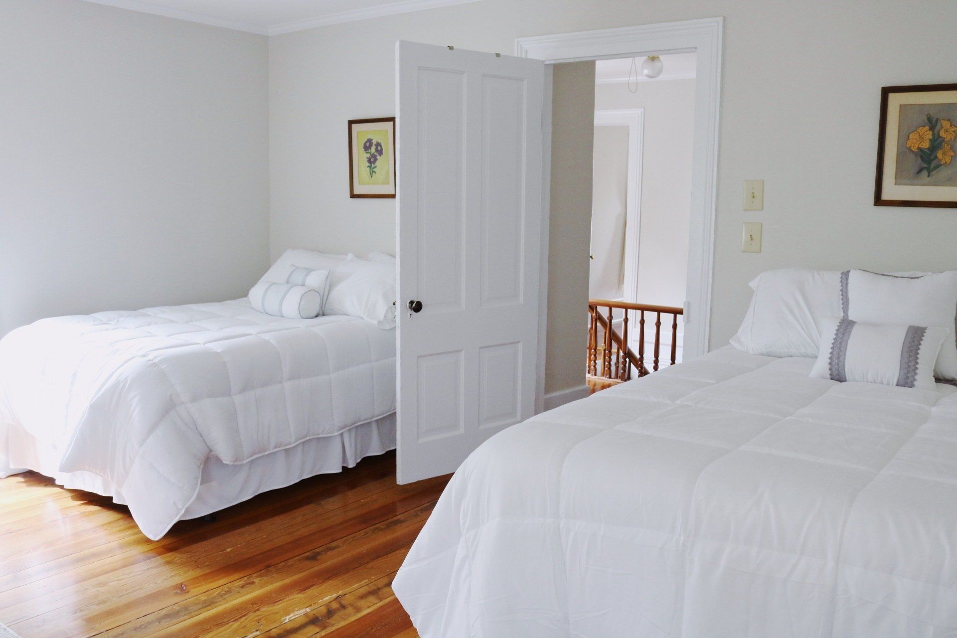 Two beds in a white-walled room with a partially open door. One bed faces the viewer. Wooden floor.