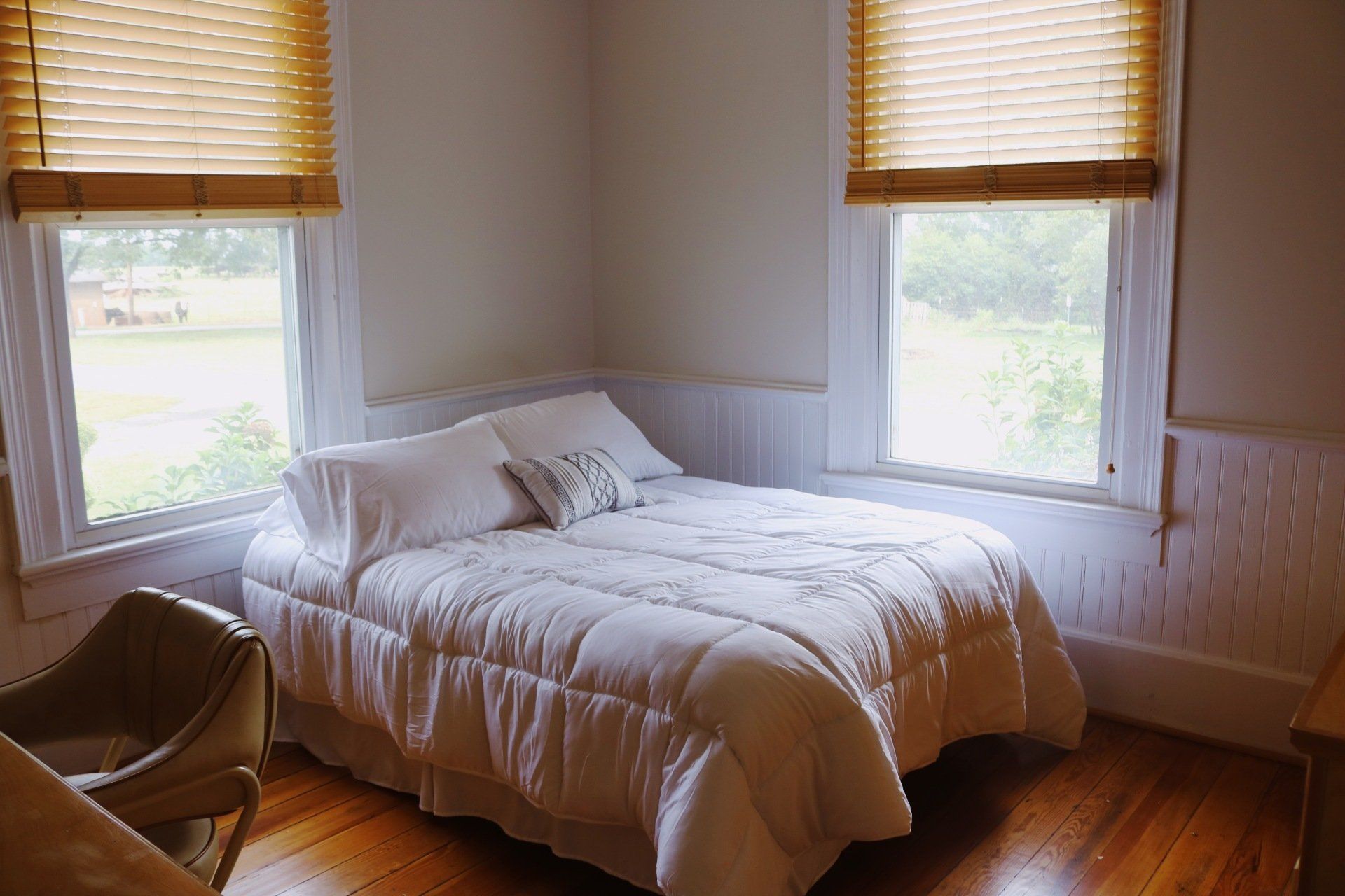 Bedroom with bed, two windows with blinds, and wooden floors.