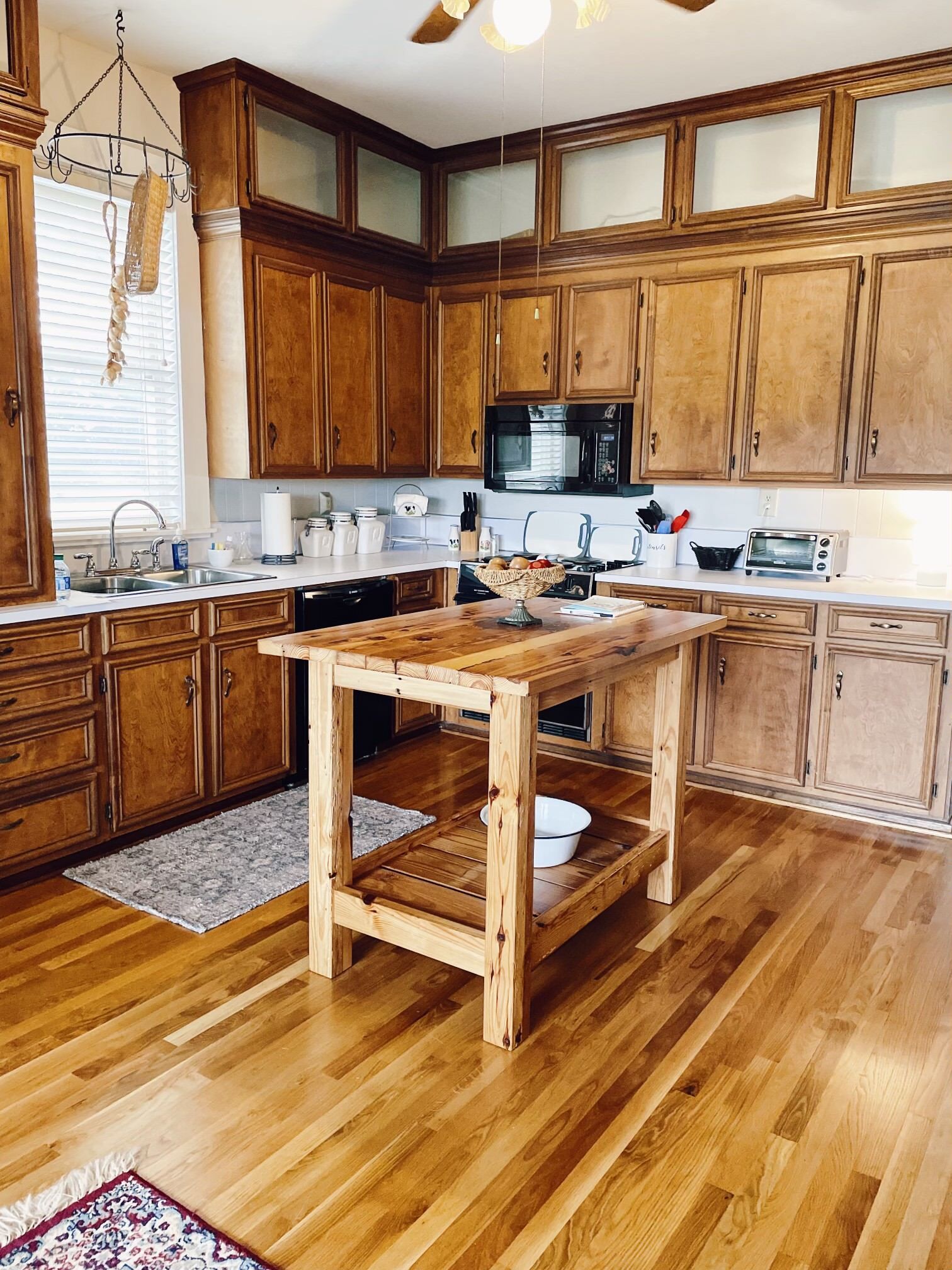 Wooden kitchen with cabinets, island, and countertops. Hardwood floors and a window are present.