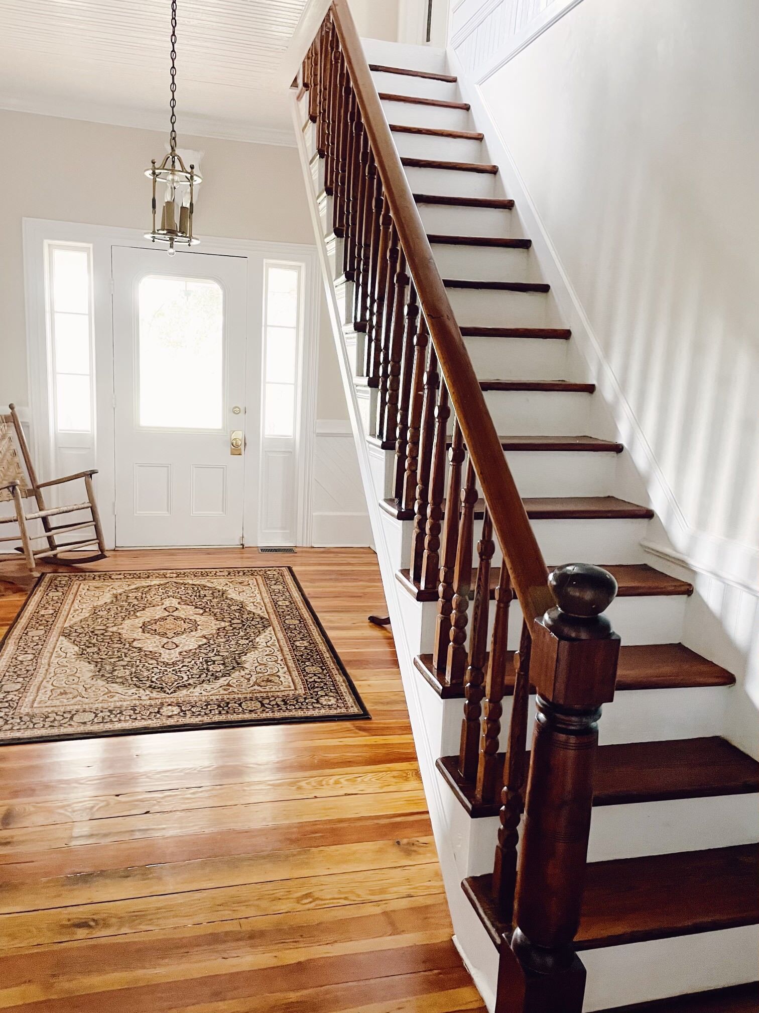 Interior with wooden stairs, ornate railing, front door, and patterned rug.