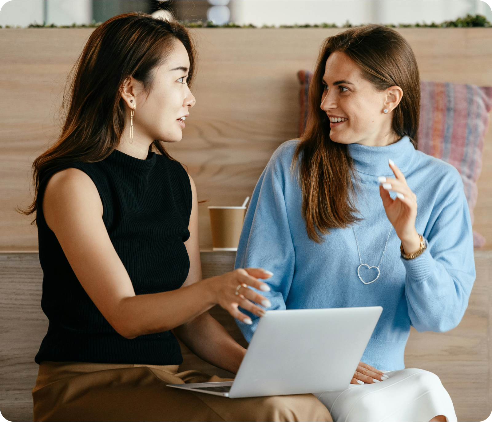 Two women are sitting next to each other with a laptop.