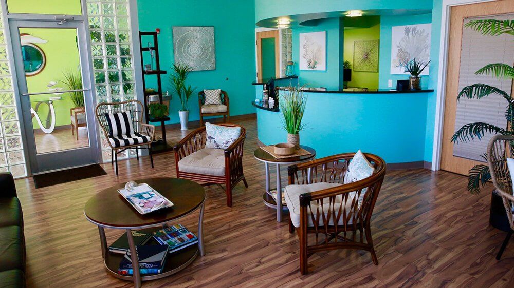 A brightly lit waiting room with turquoise walls and wooden furniture.