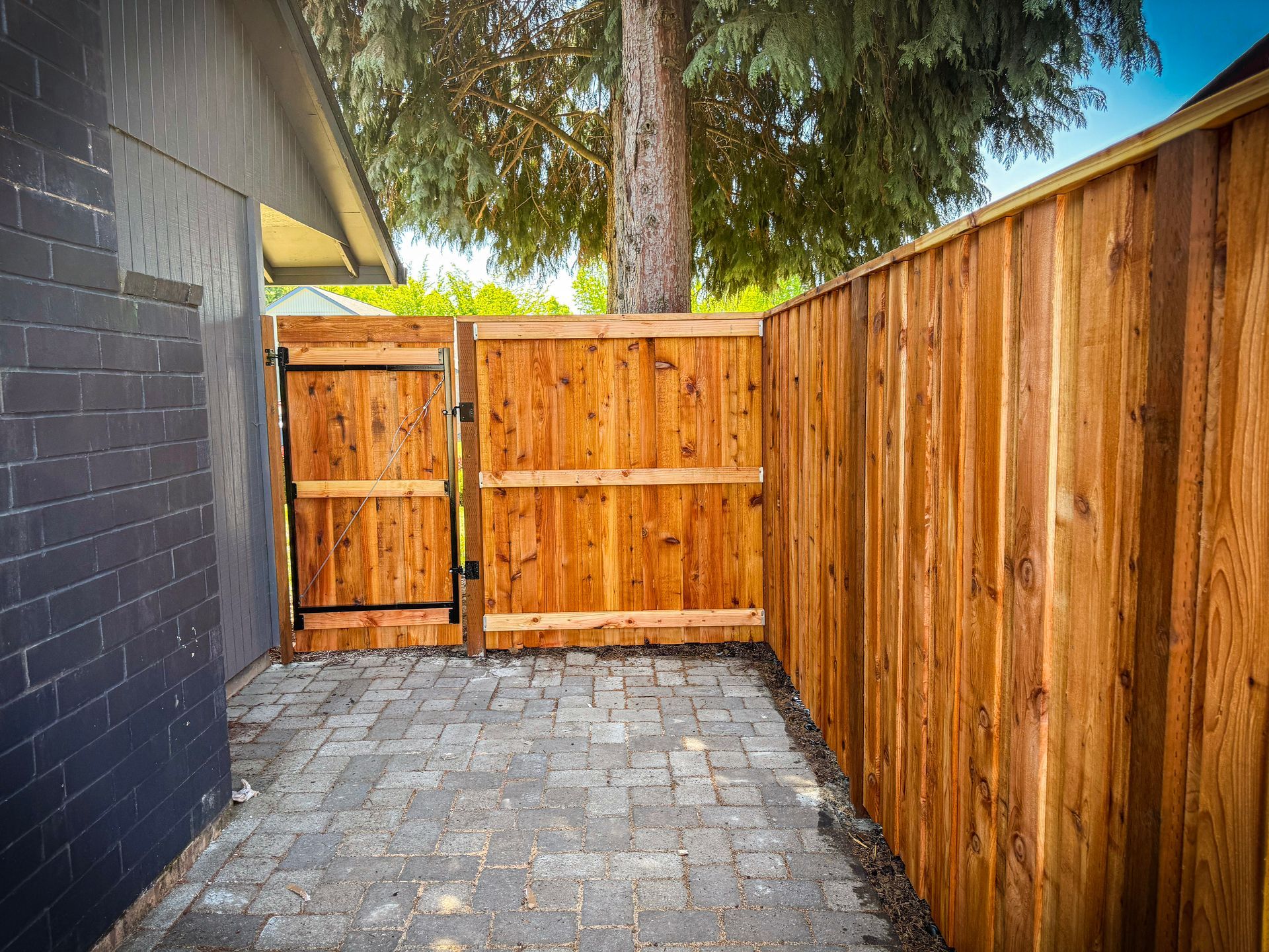 Wooden gate and fence enclose a brick-paved patio area; a tree is visible in the background.