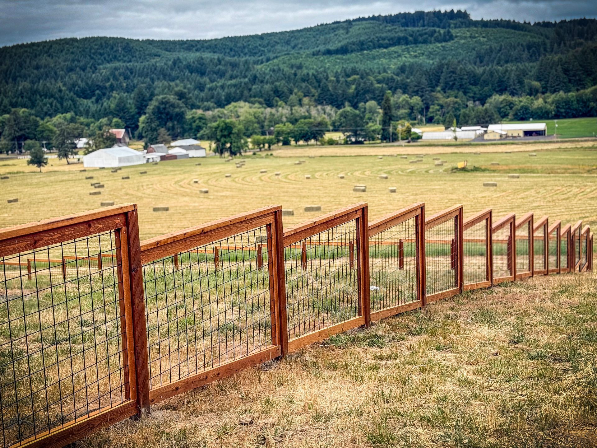 Rustic fence in field, with rolling hills and trees in the background under an overcast sky.