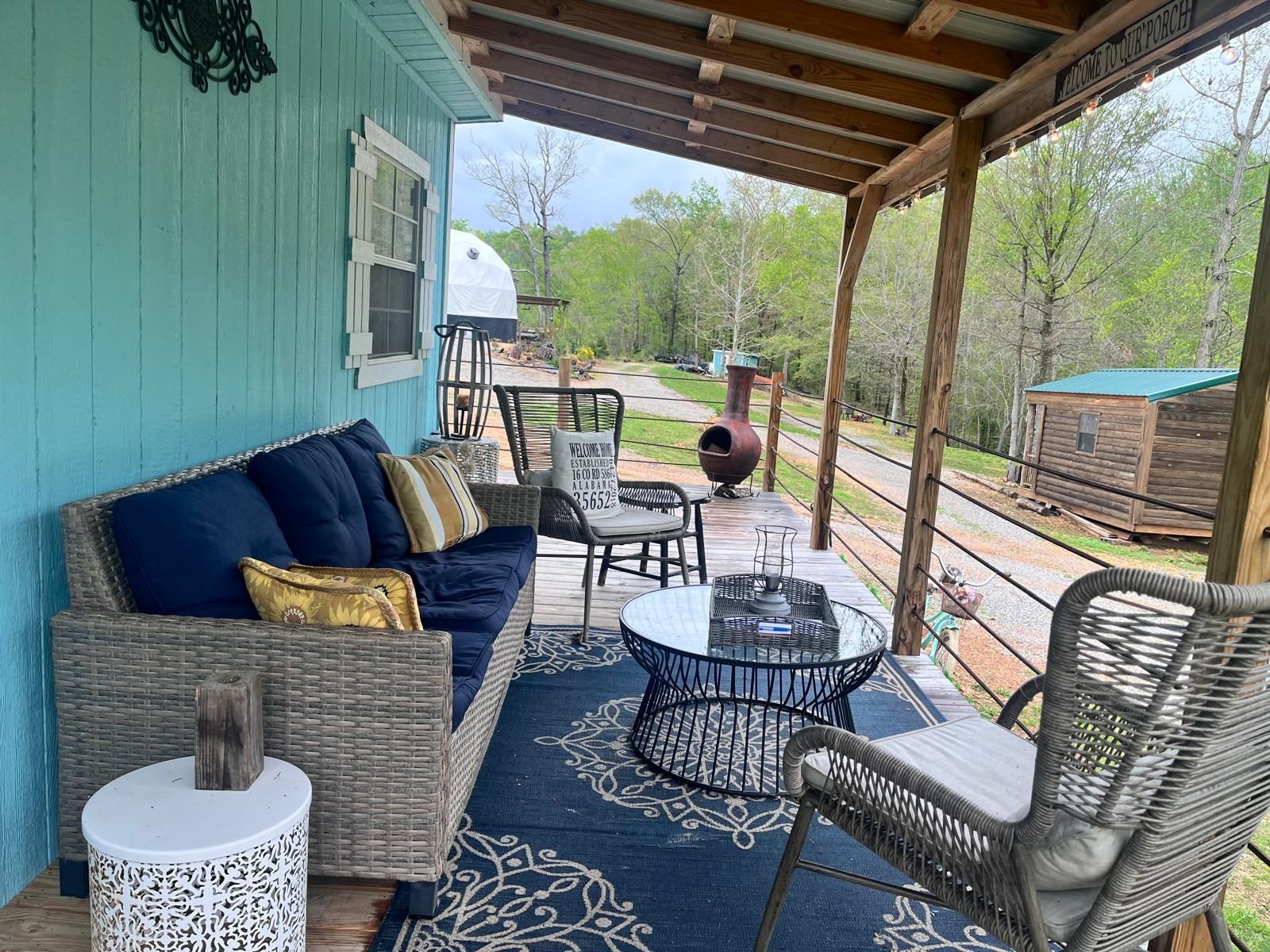 Porch with blue walls, wicker furniture, and a rug. Overlooks a path and trees.