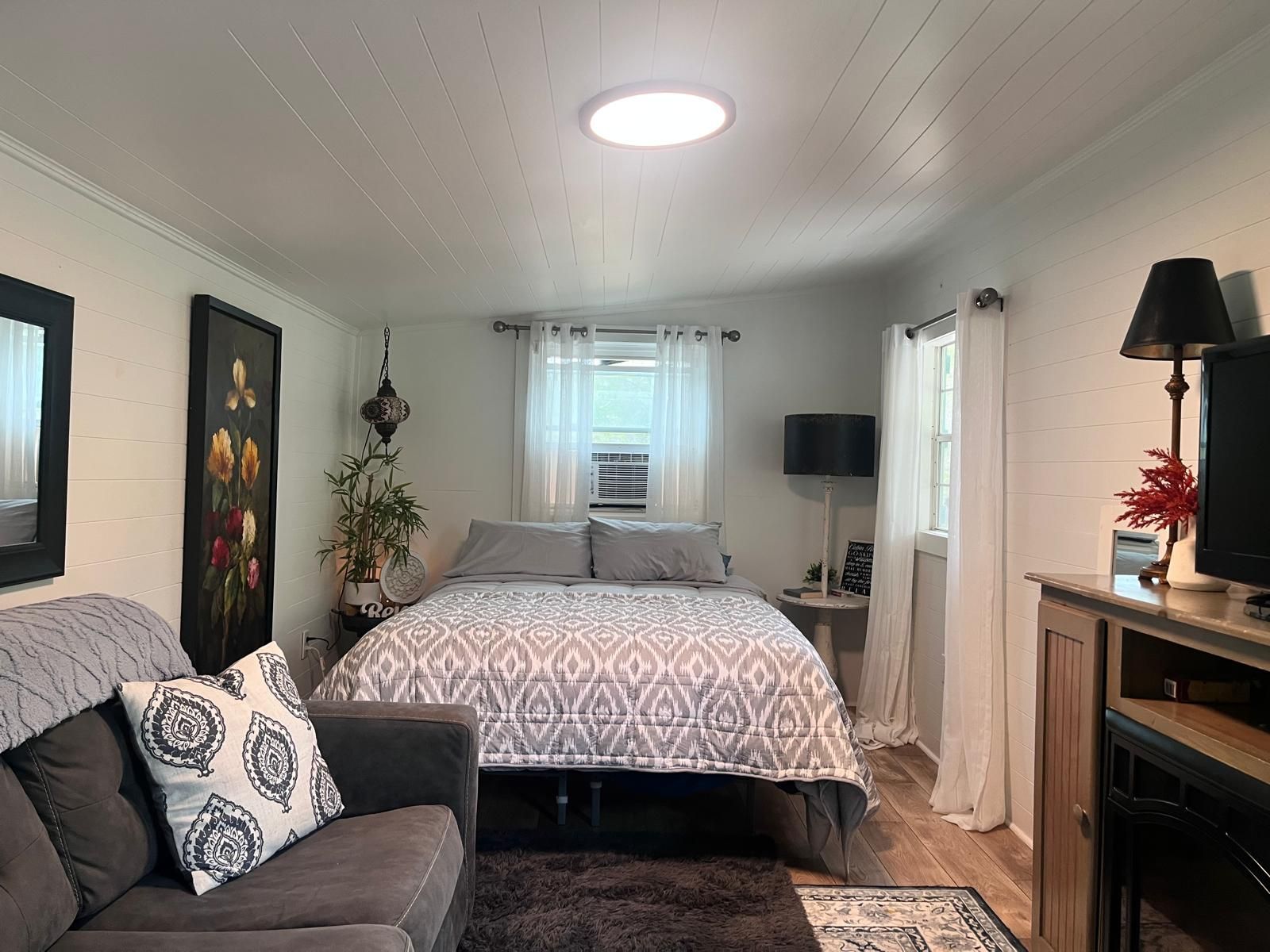 Cozy bedroom with bed, small sofa, TV, and natural light from a skylight.