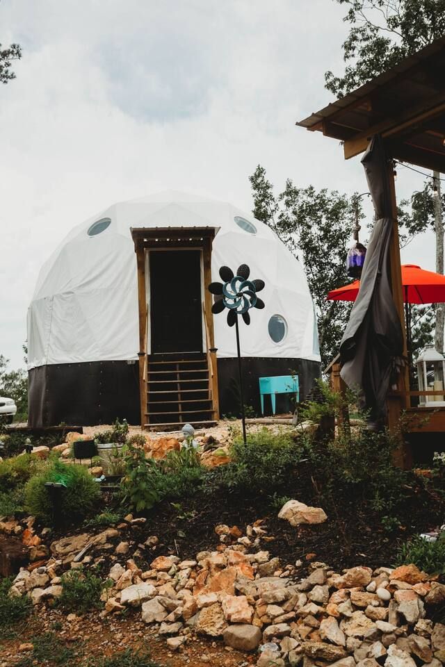 White geodesic dome with blue accents, wooden steps, and a decorative wind spinner.