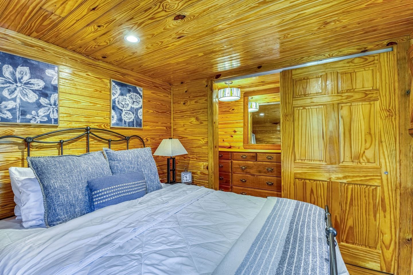 Bedroom with wooden walls, bed with blue bedding, and floral artwork.