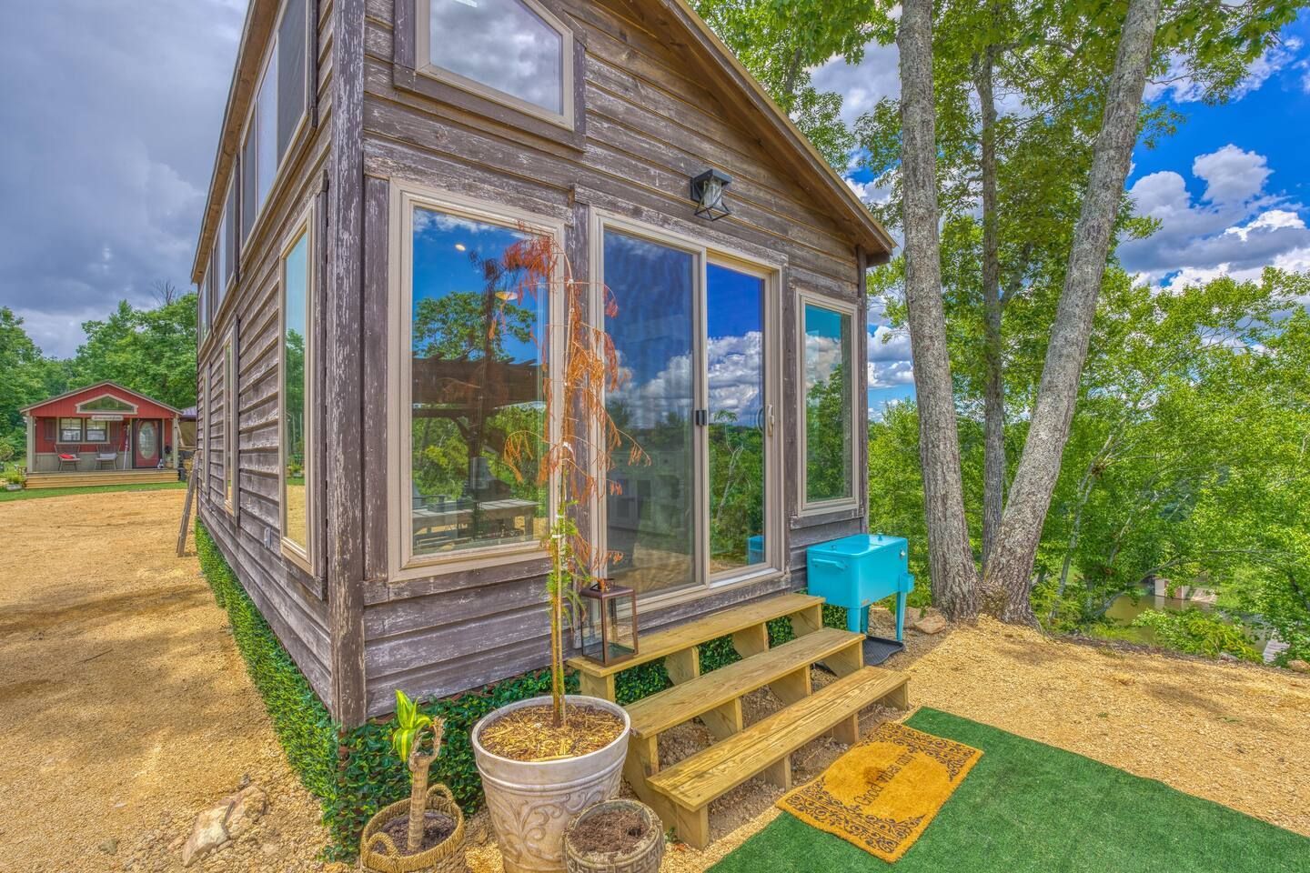 Wooden cabin with glass sliding doors, small steps, and a blue cooler outdoors.