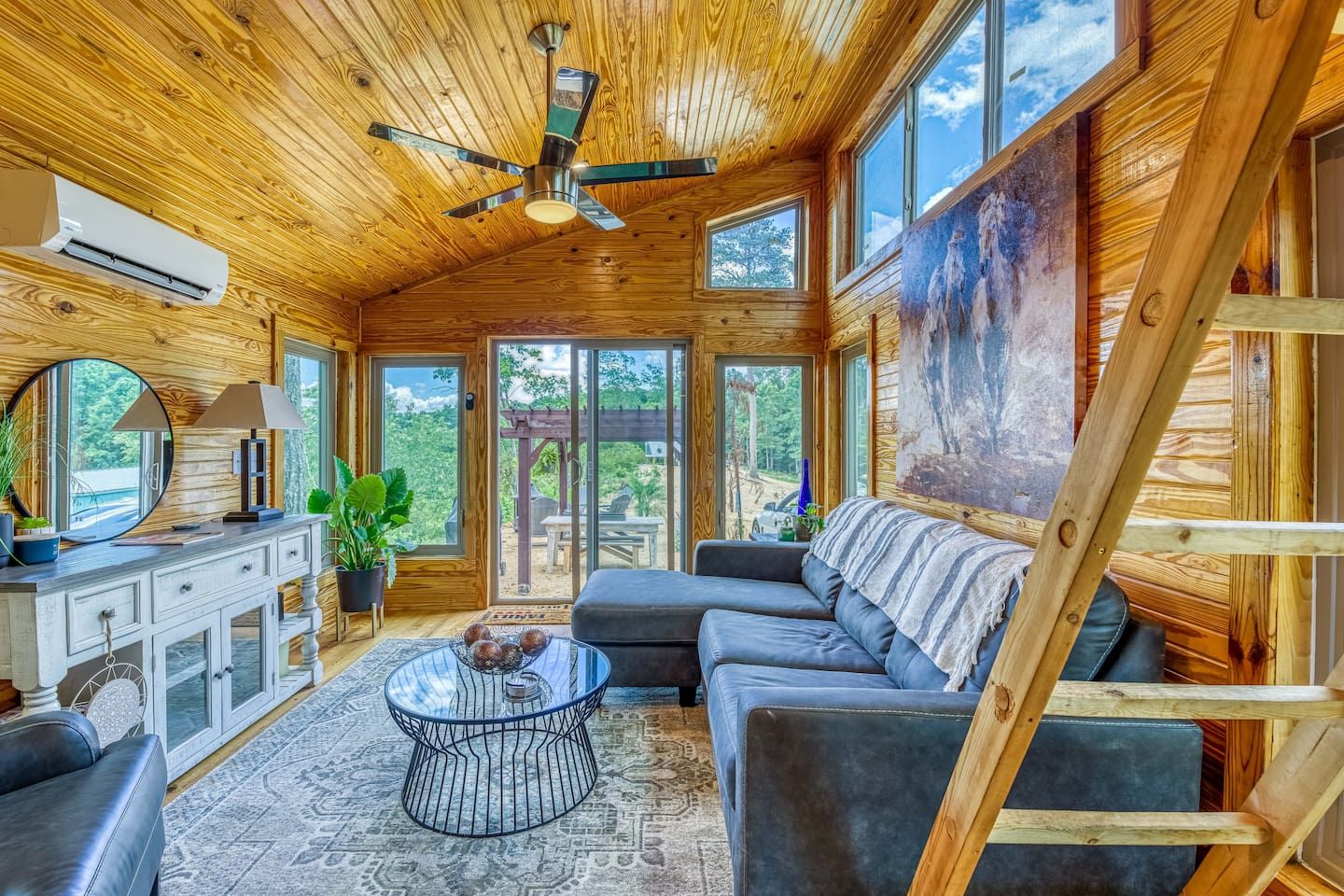 Living room with wooden paneling, sectional sofa, and ladder to loft.