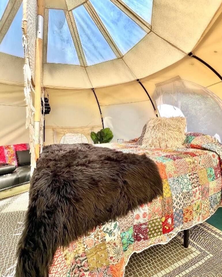 Cozy glamping tent interior with bed, patchwork quilt, and shaggy throw rug.