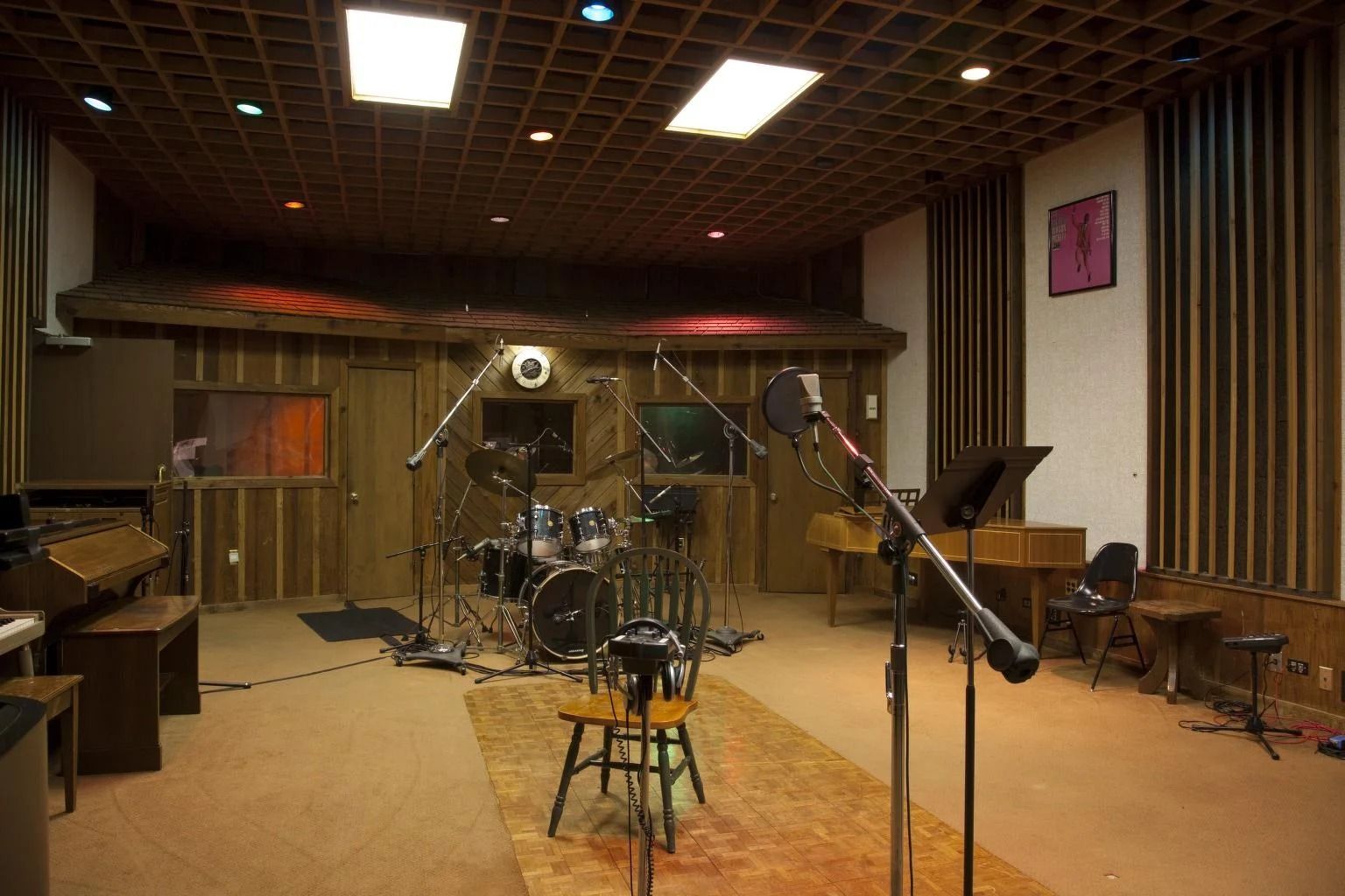 Recording studio with drums, microphones, and soundproofing, brown and beige tones.