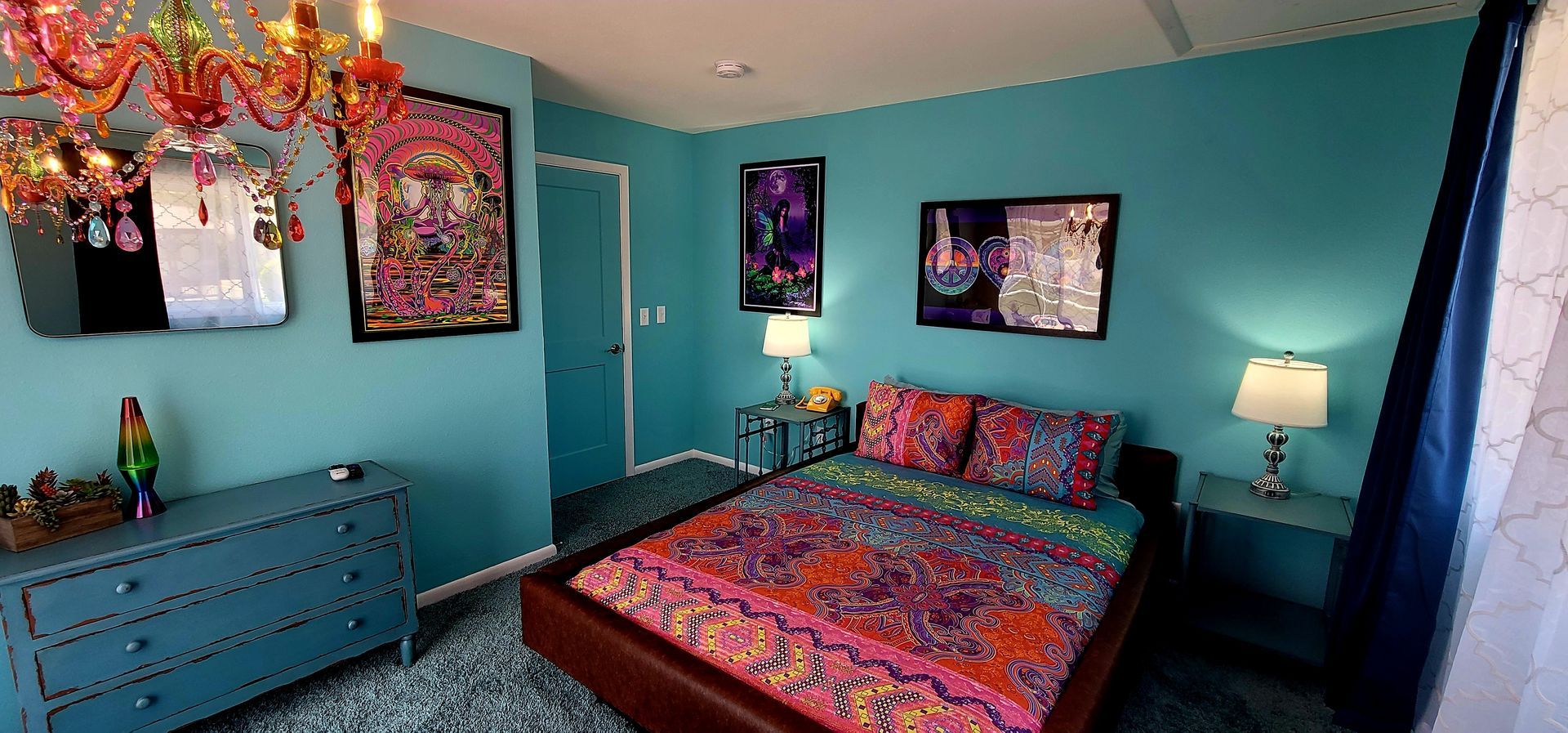 A teal bedroom with a bed, dresser, and wall art. A chandelier hangs from the ceiling. And a King waterbed
