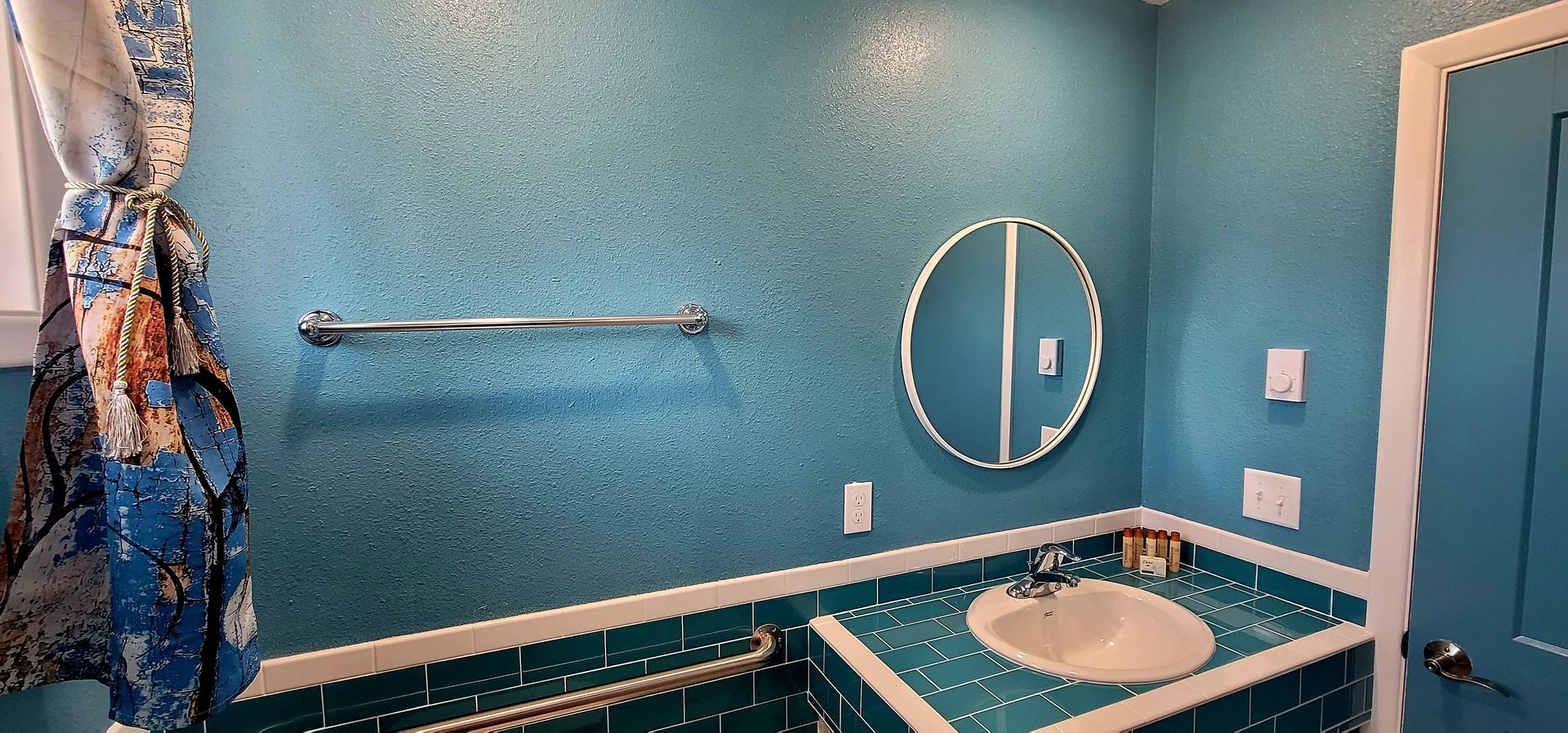 Teal-tiled bathroom with round mirror, chrome towel rack, and a white sink.