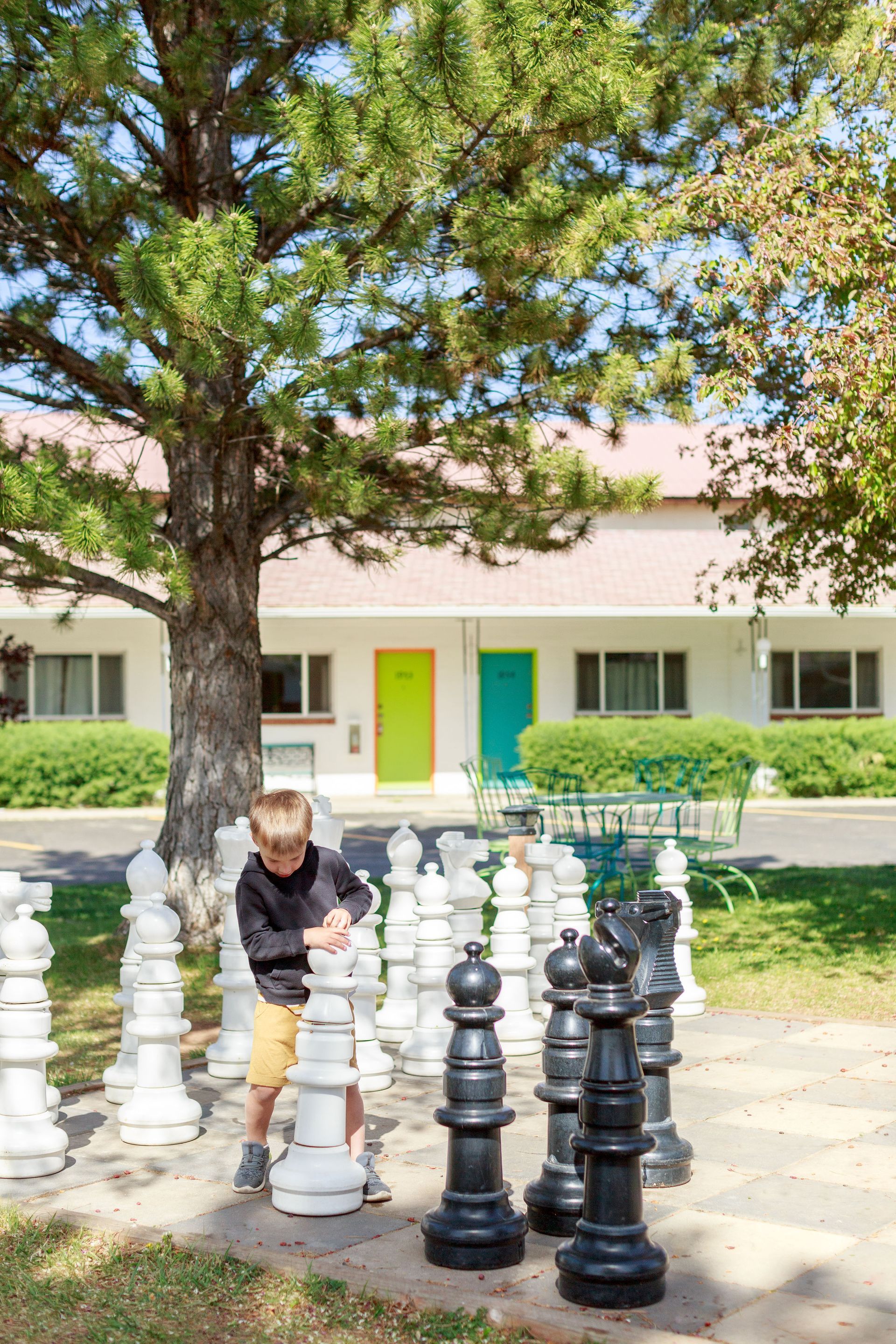 Child playing giant chess outdoors, white and black life sized pieces, motel in background.