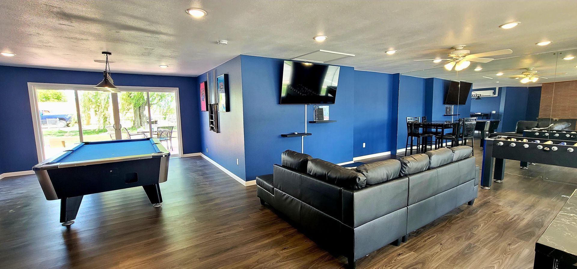 A recreation room with a pool table, dark blue walls, a leather sofa, and a foosball table.
