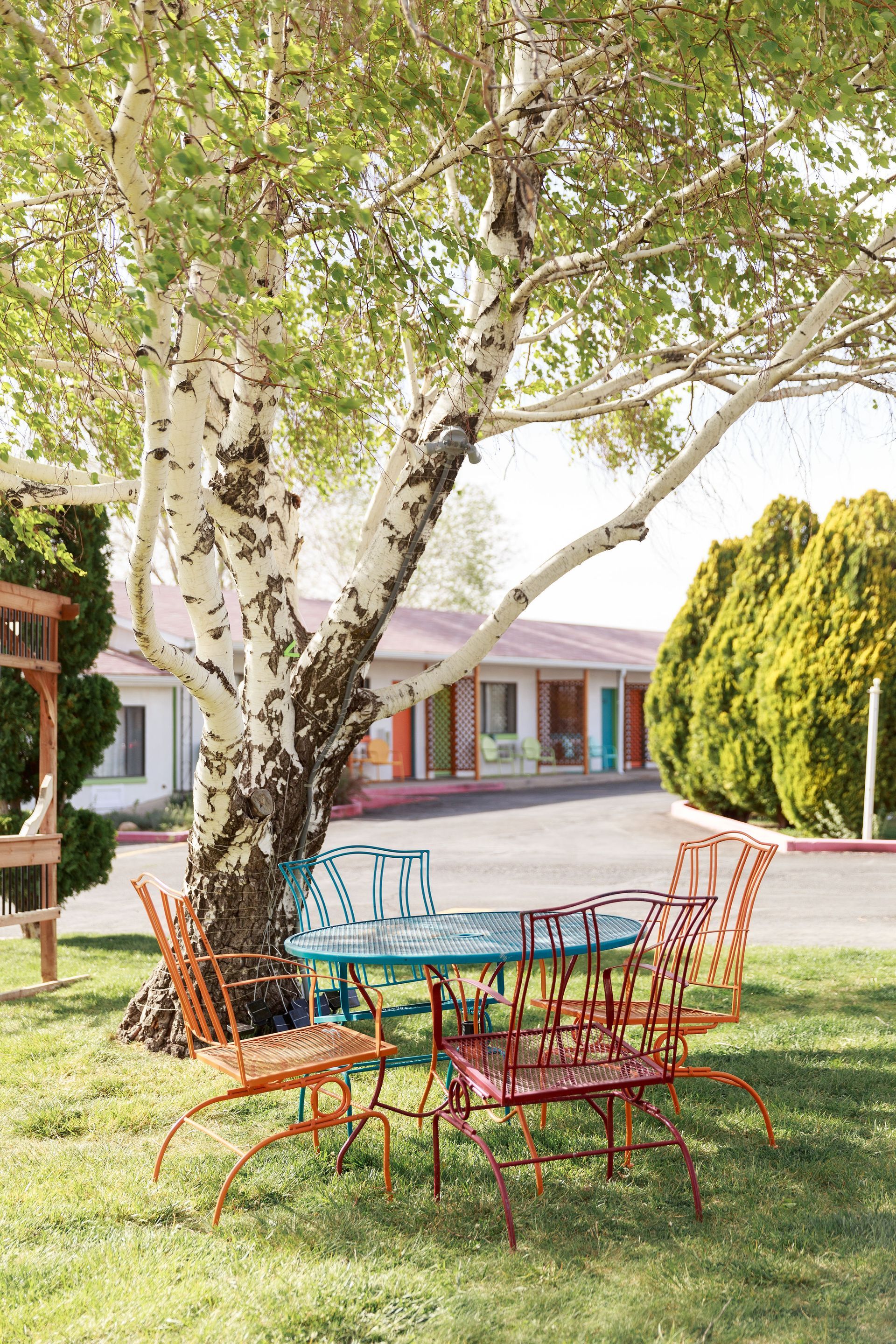 Colorful metal chairs and table under a tree in front of a motel with bright doors.