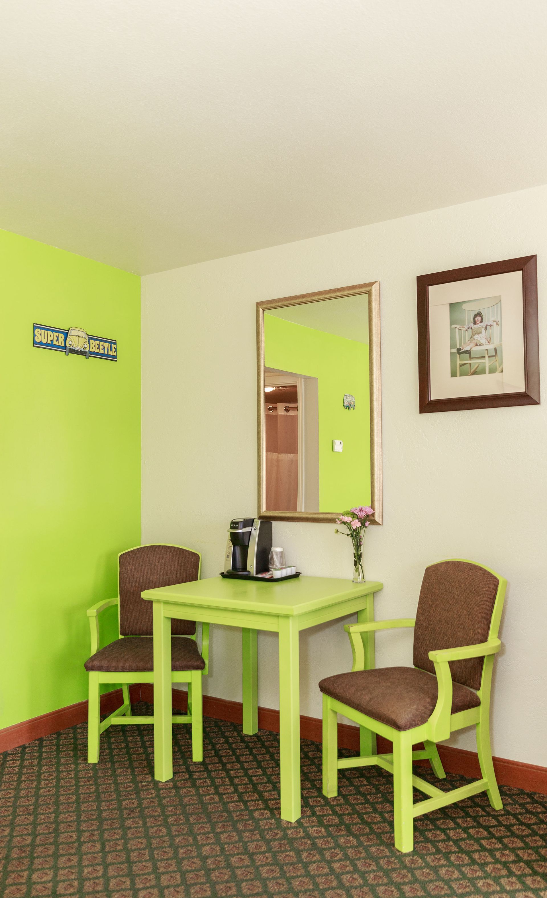 A table and two chairs in a motel room with green accents.