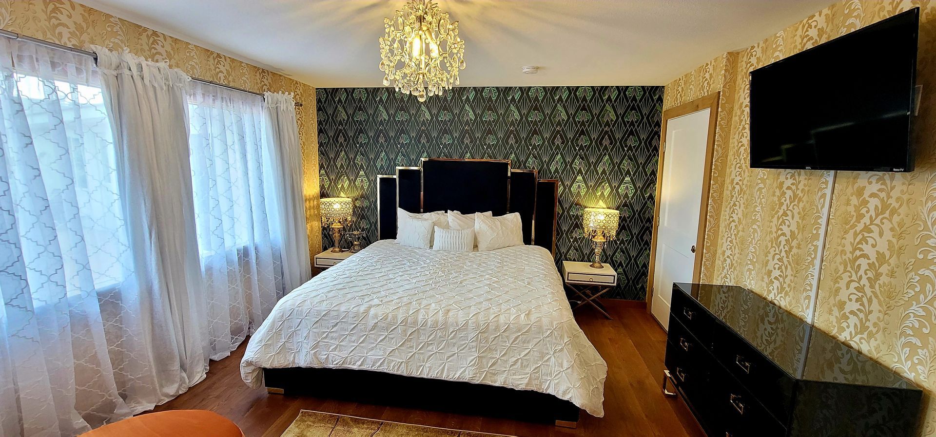 Bedroom with a California King bed, TV, dresser, window, chandelier, and a decorative green wall.