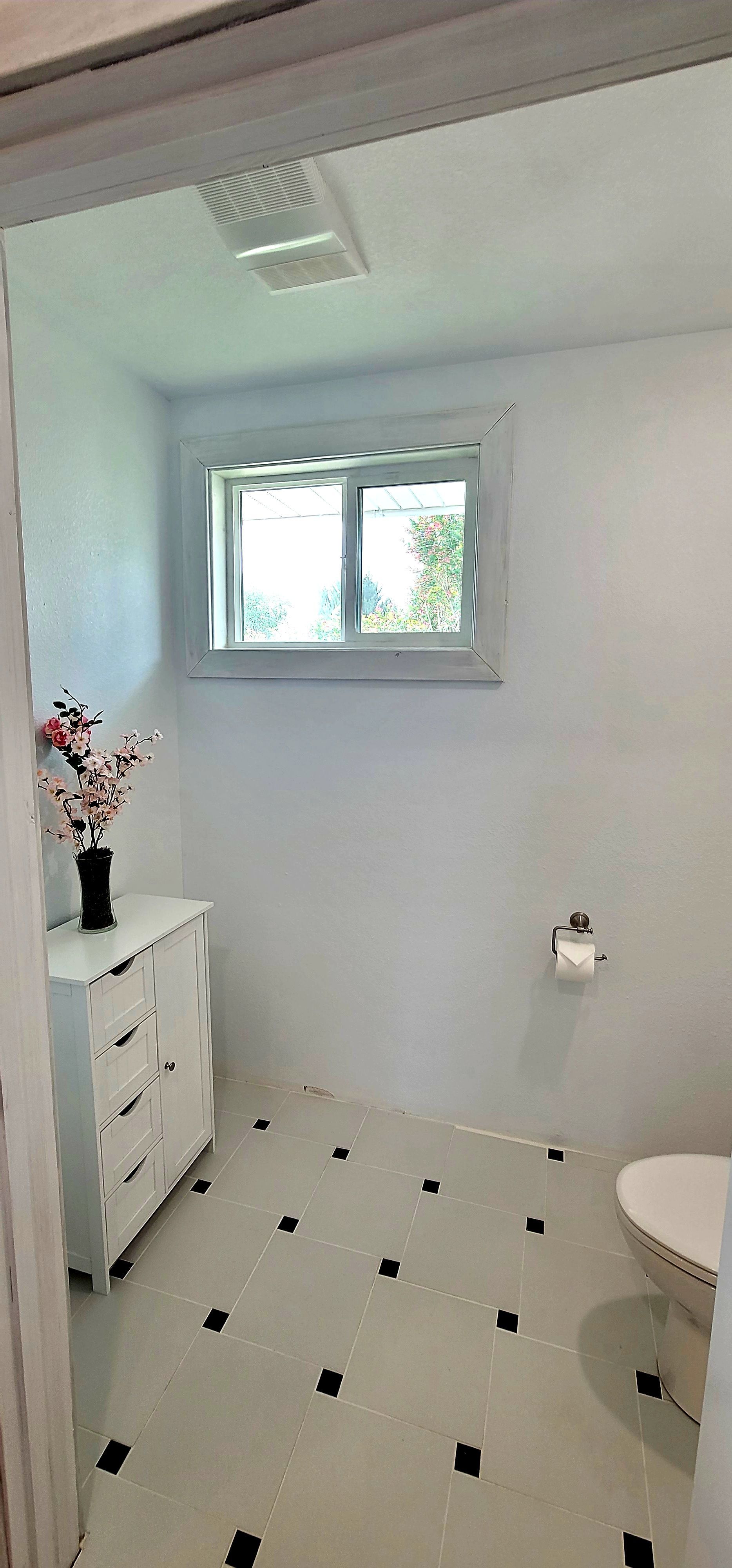 white bathroom with black tile accents, a window, and a white dresser.