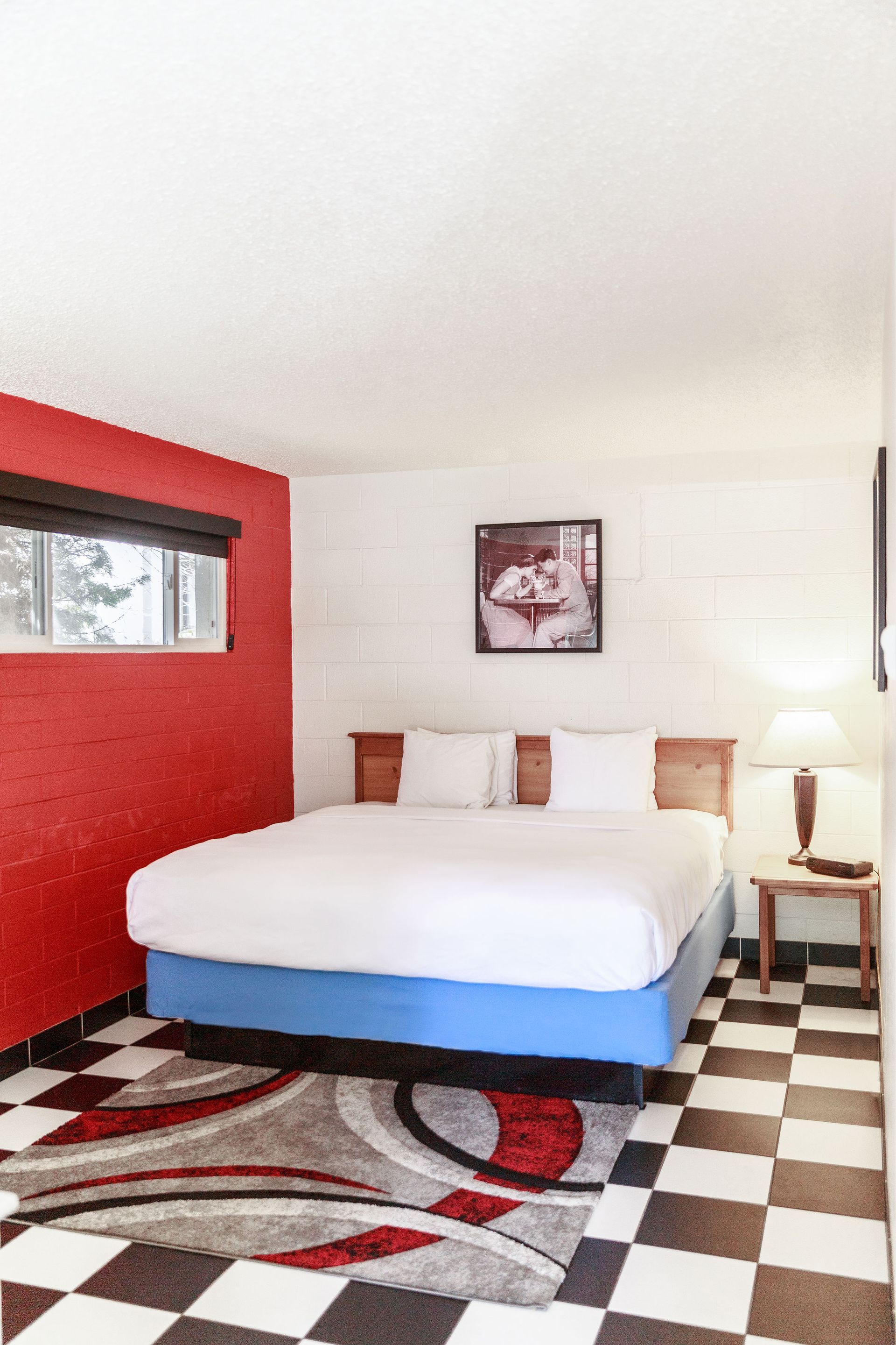 Hotel room with a King bed, red accent wall, checkered floor, and colorful rug.