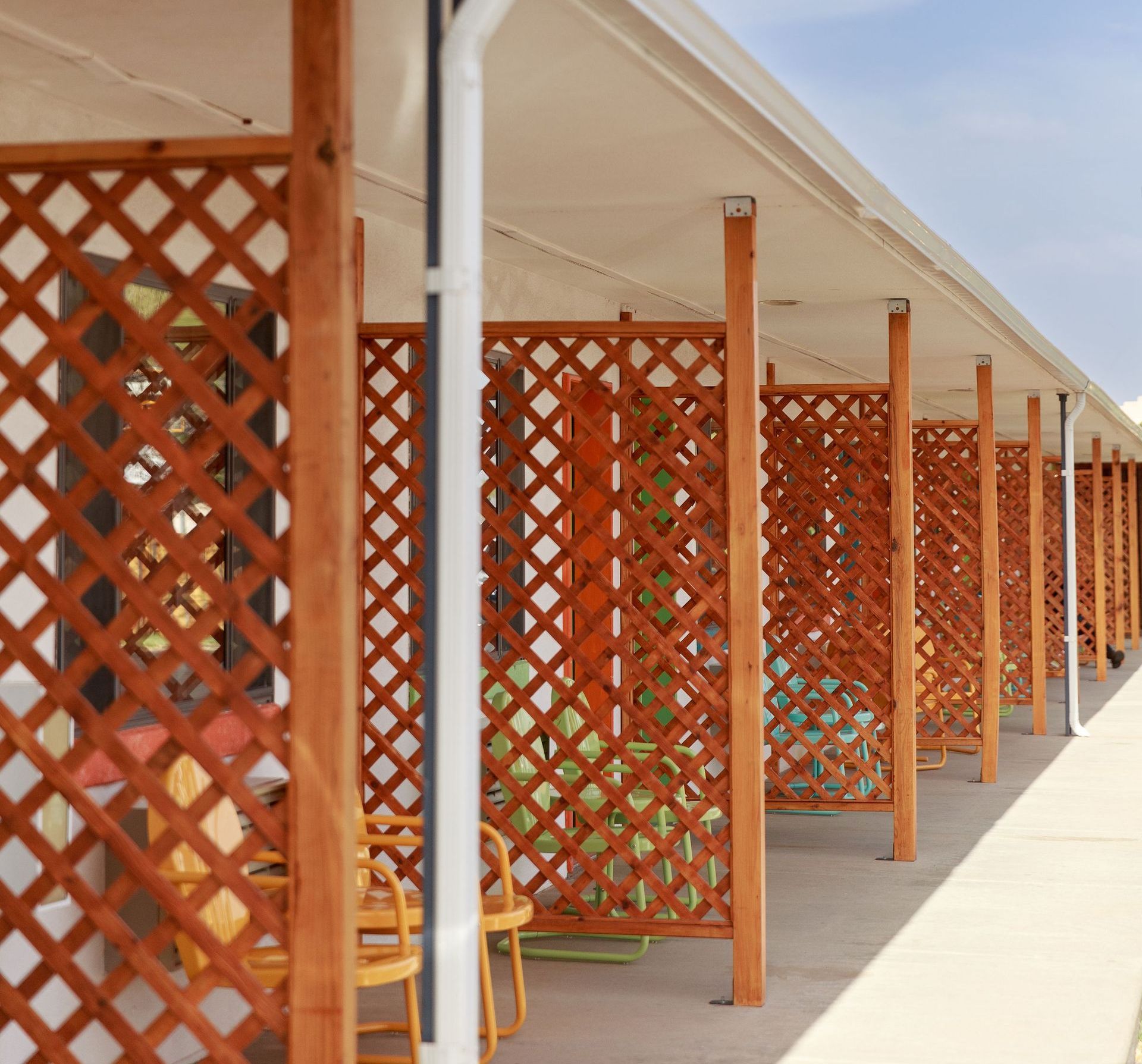 Row of lattice-screened outdoor seating, brown wood, under a white awning separating rooms.
