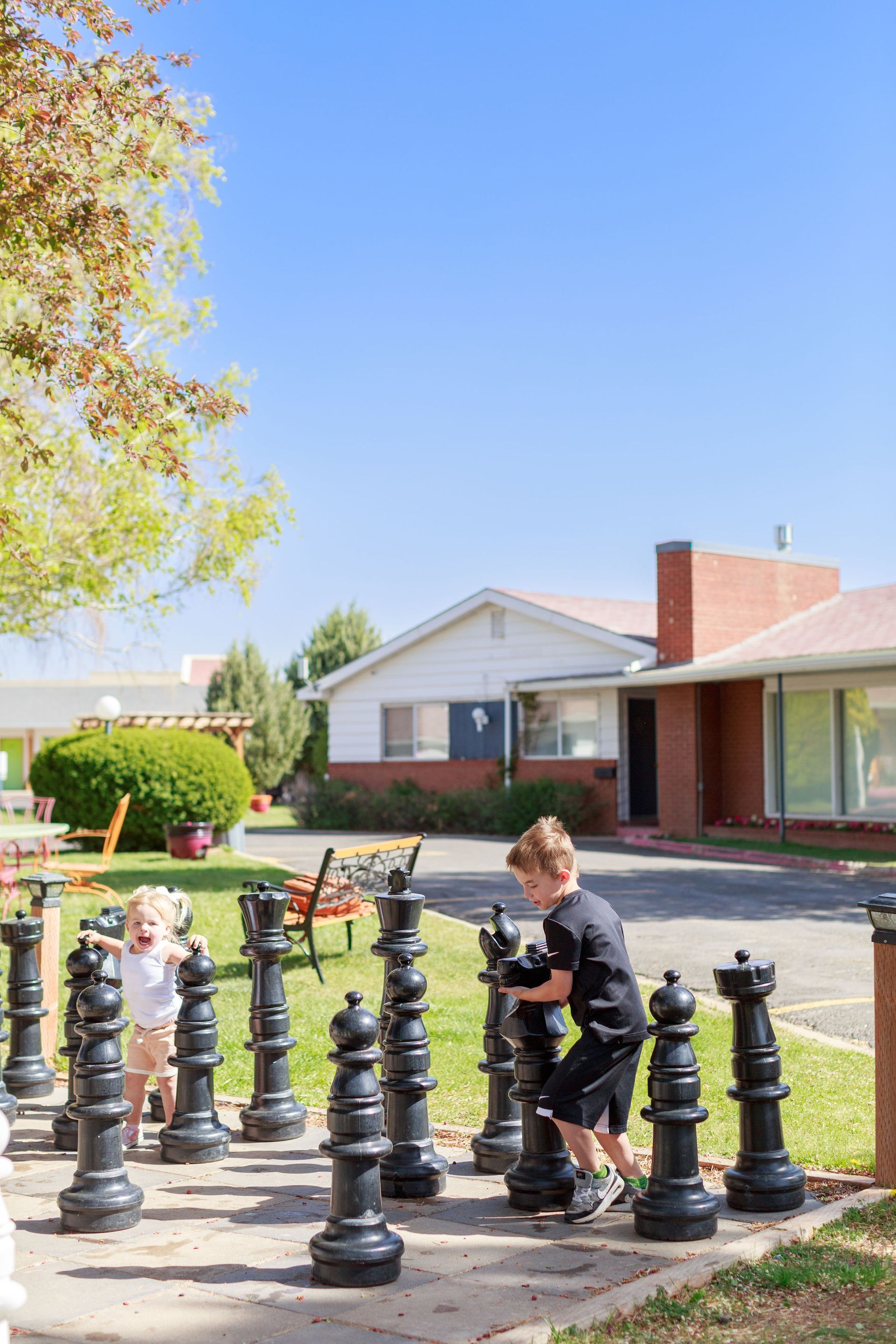 Two children playing with giant life sized chess pieces in the Retro Inn courtyard on a sunny day.