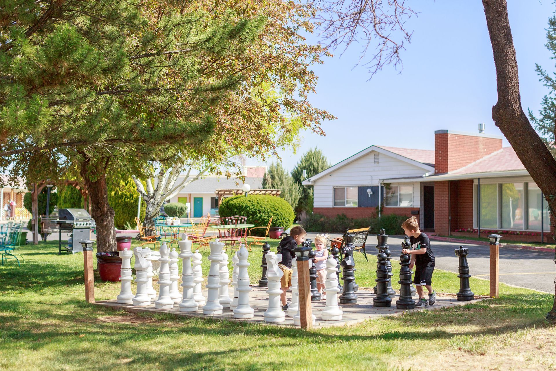 Two children playing chess with life soutdoor chess pieces in a park setting.