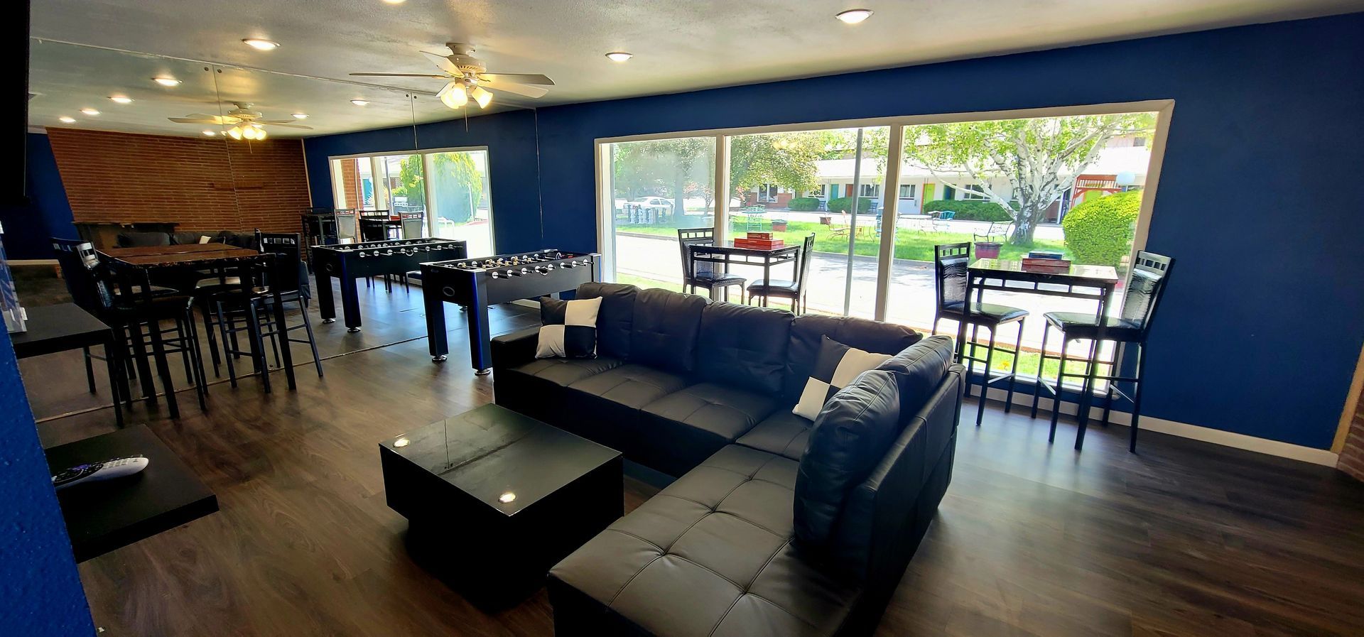 A blue-walled game room with a sectional sofa, a foosball table, pool table, video games, and an outdoor view.