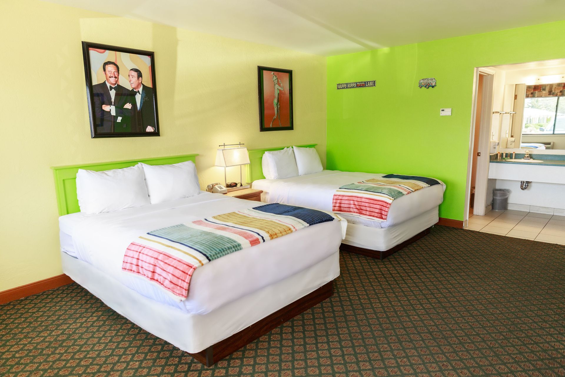Motel room with two beds, green walls, framed art, and an open bathroom.