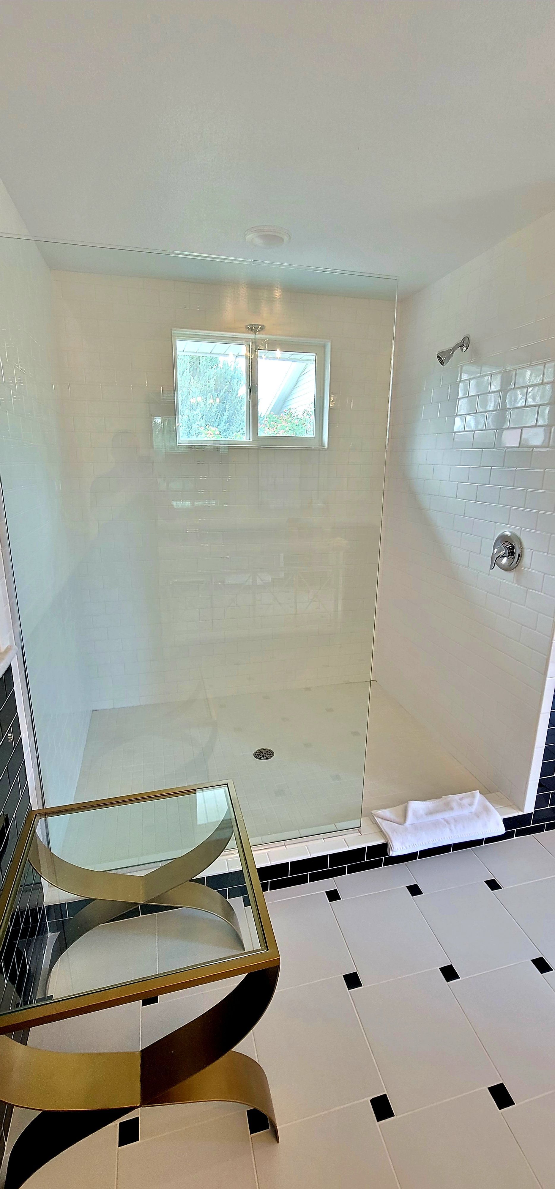 Bathroom with a glass-enclosed shower, white tile, and gold accent chair on black and white tile floor  in the Great Gatsby bathroom.
